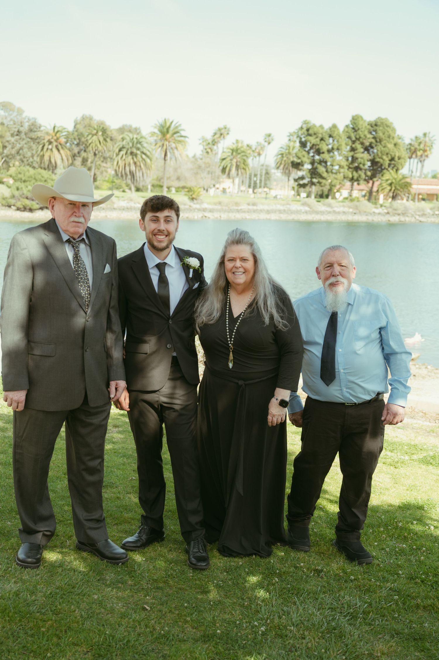 Family group of four poses outdoors near a lake at a wedding, dressed in formal attire.