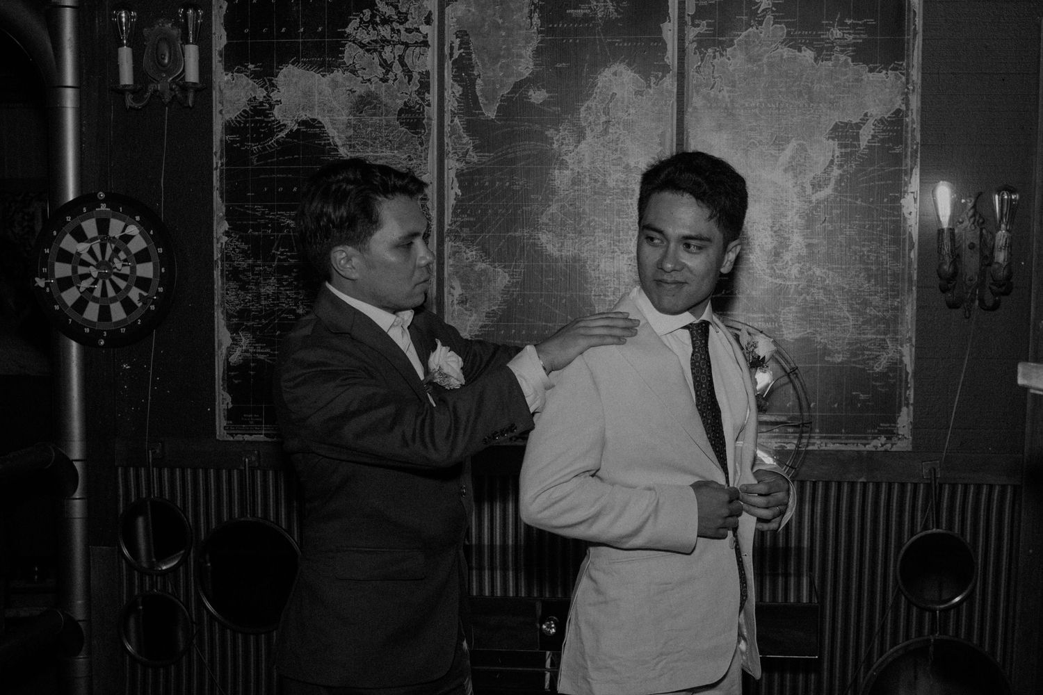 Groomsman adjusts grooms tie before wedding ceremony in black and white photo.