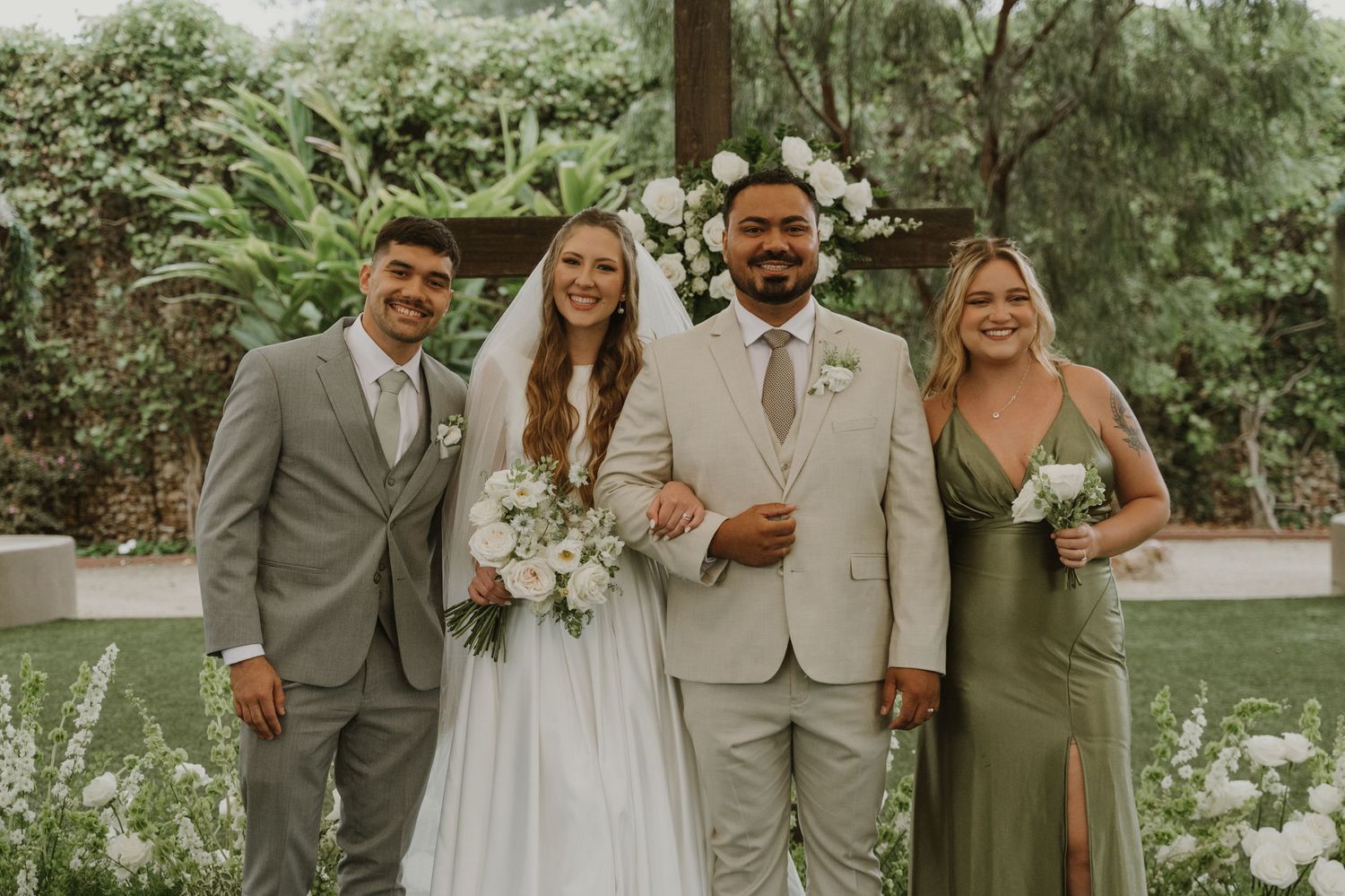 Wedding party poses outdoors with bride, groom, groomsman, and bridesmaid in sage green dress.