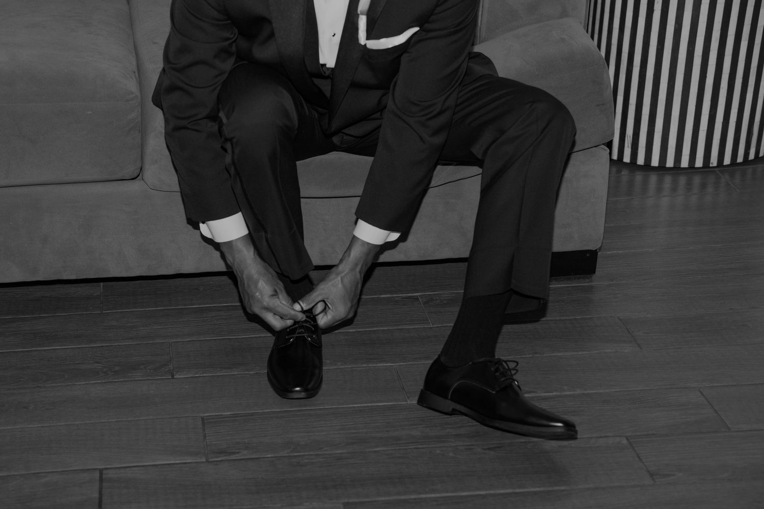 Man in suit tying dress shoes while seated on a couch, black and white photo.