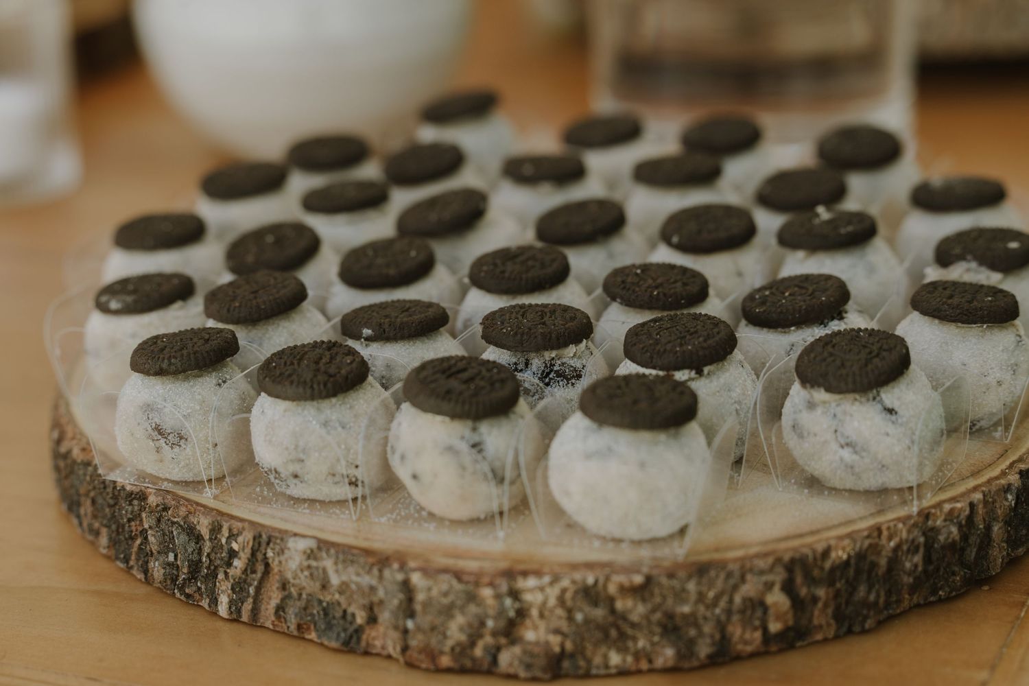 Oreo truffle cake pops displayed on a rustic wooden slice serving board at a wedding reception.