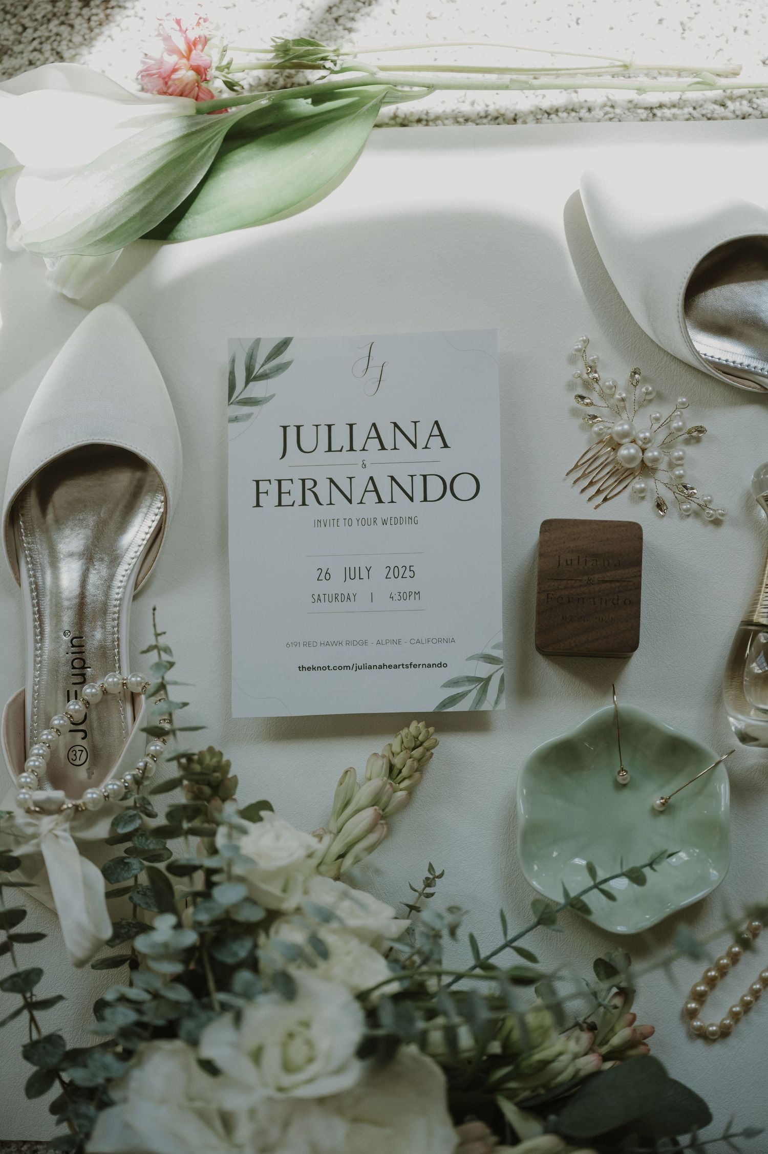 Elegant wedding flat lay featuring invitation for Juliana and Fernando, bridal shoes, floral hair comb, and eucalyptus greenery.
