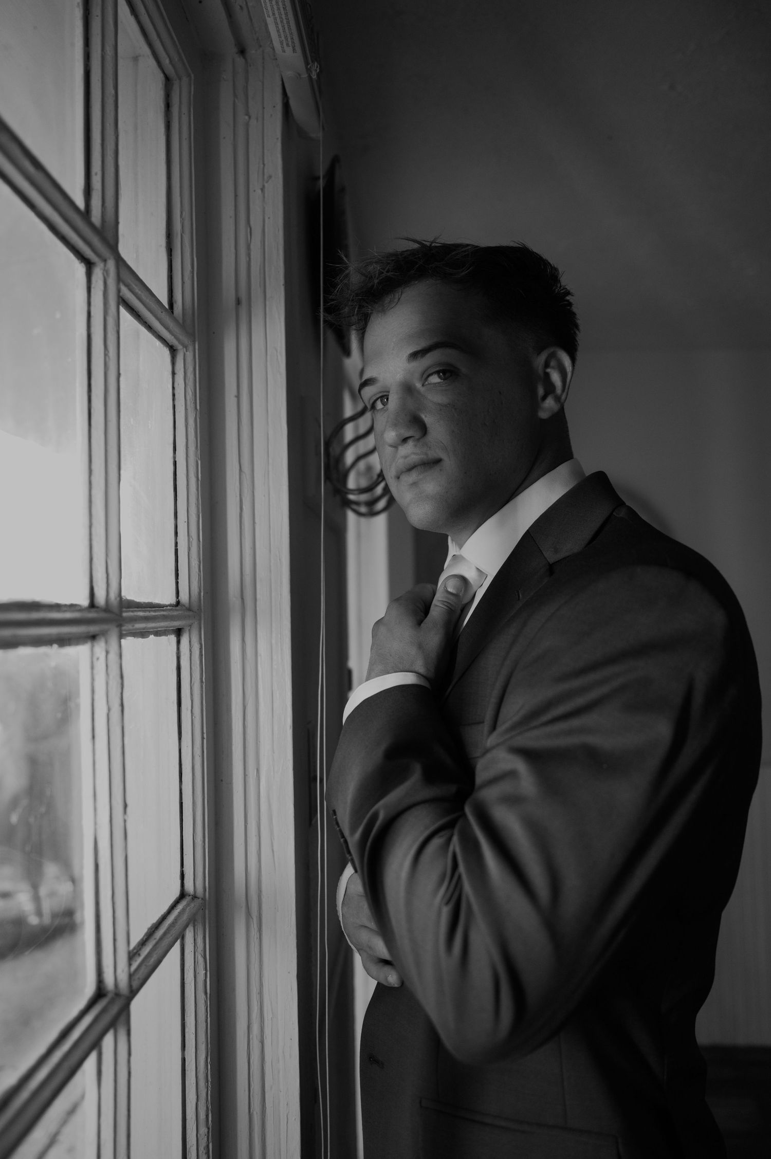 Dramatic black and white portrait series taken by a window with moody lighting.