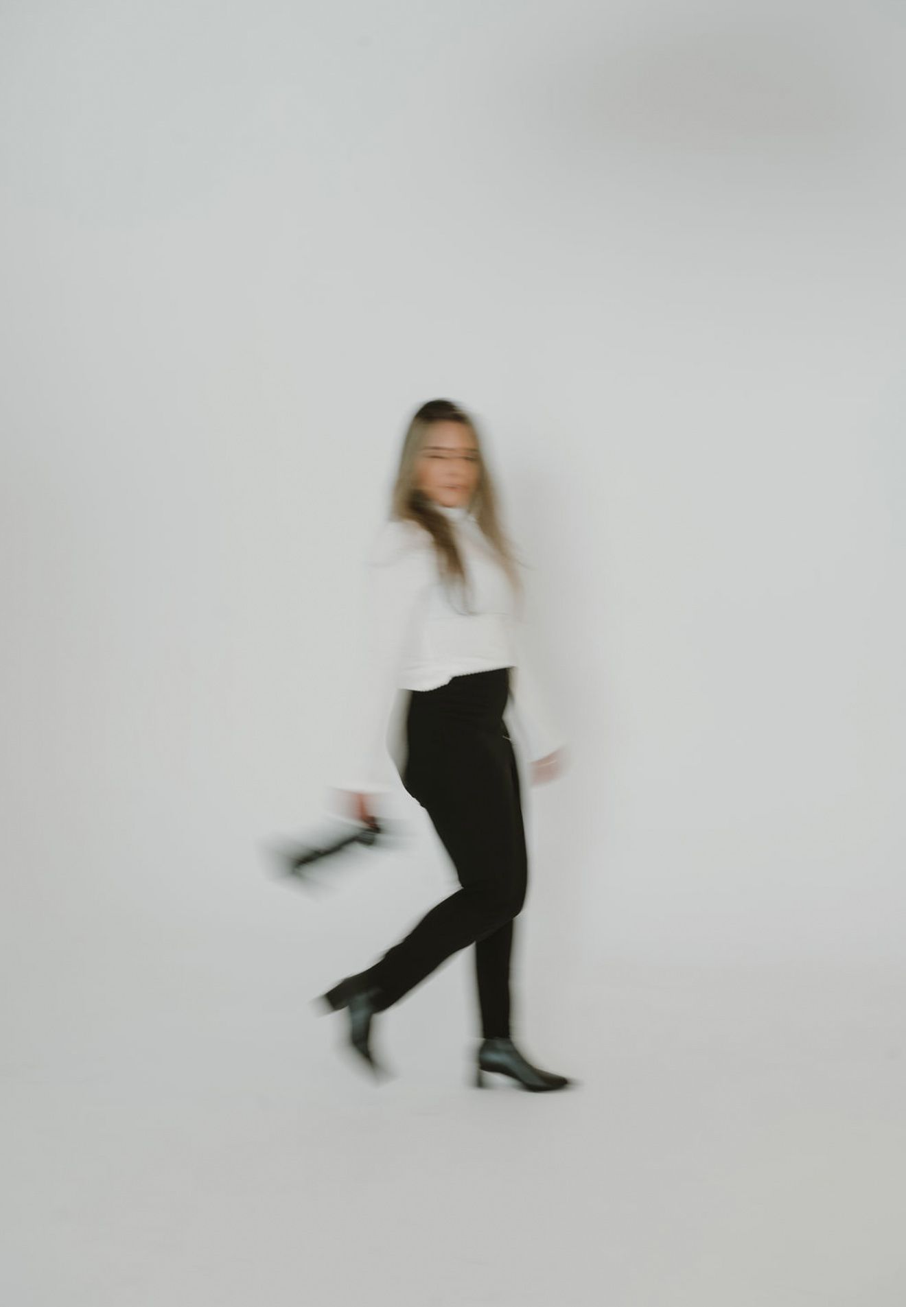 Artistic blurred motion portrait in minimalist white studio setting.