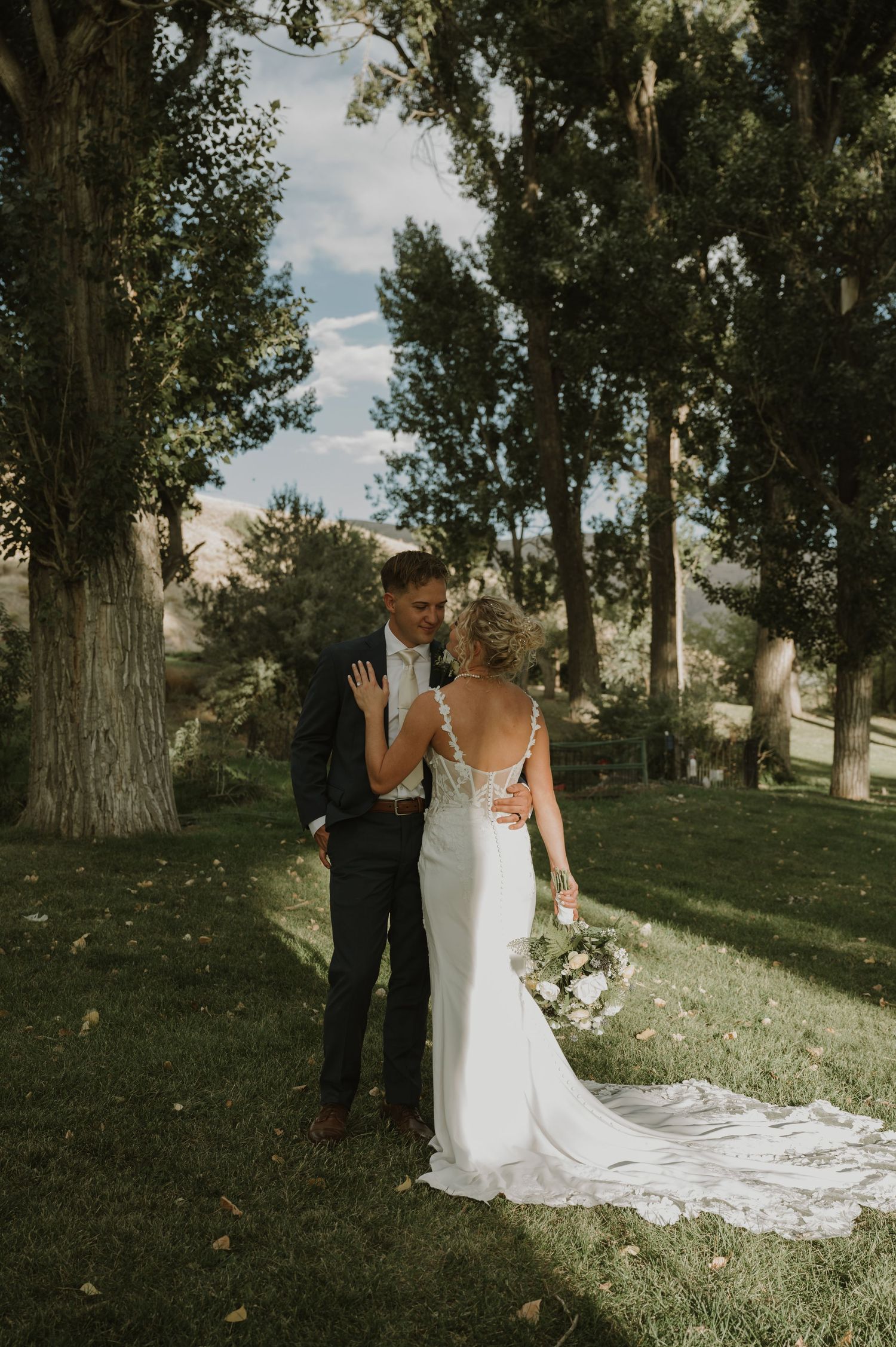 Elegant wedding couple poses among tall trees in an outdoor setting.