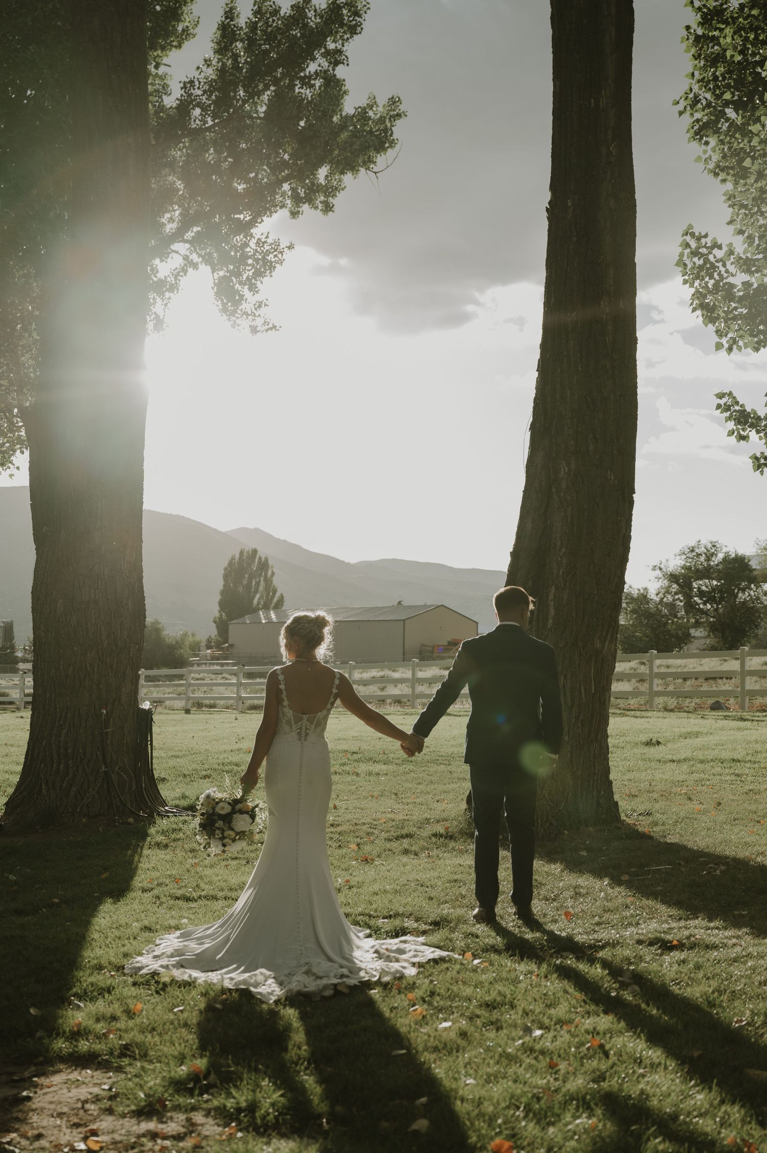 A backlit wedding photo with sunlight streaming through trees creating a dreamy silhouette.
