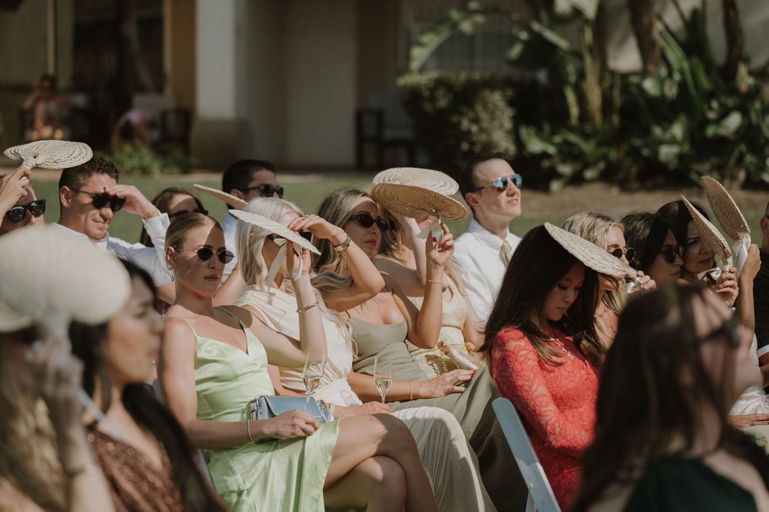 Wedding guests shielding eyes from sun during outdoor ceremony.