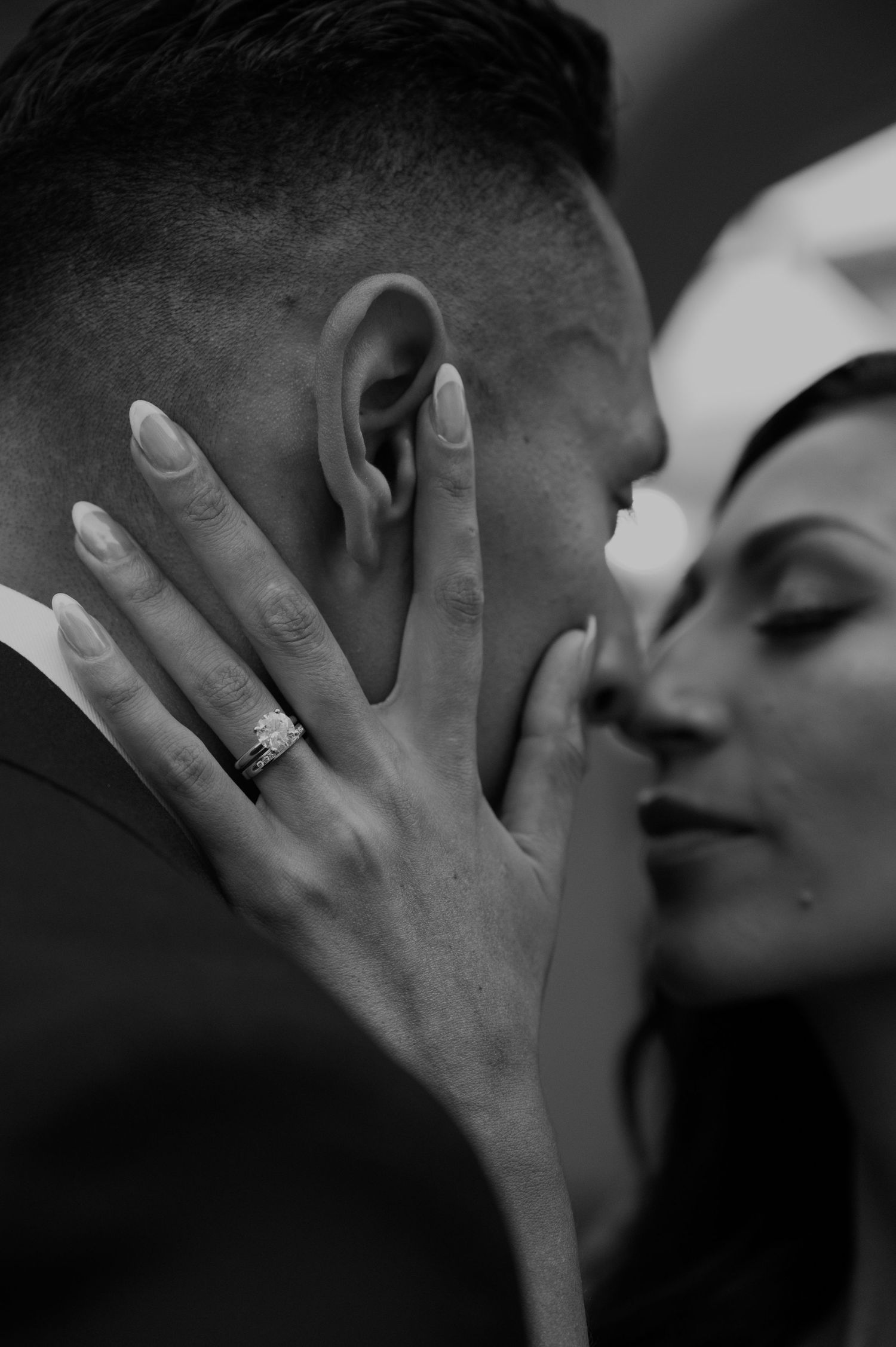 A black and white intimate photo of a couple sharing a tender moment with an engagement ring visible.