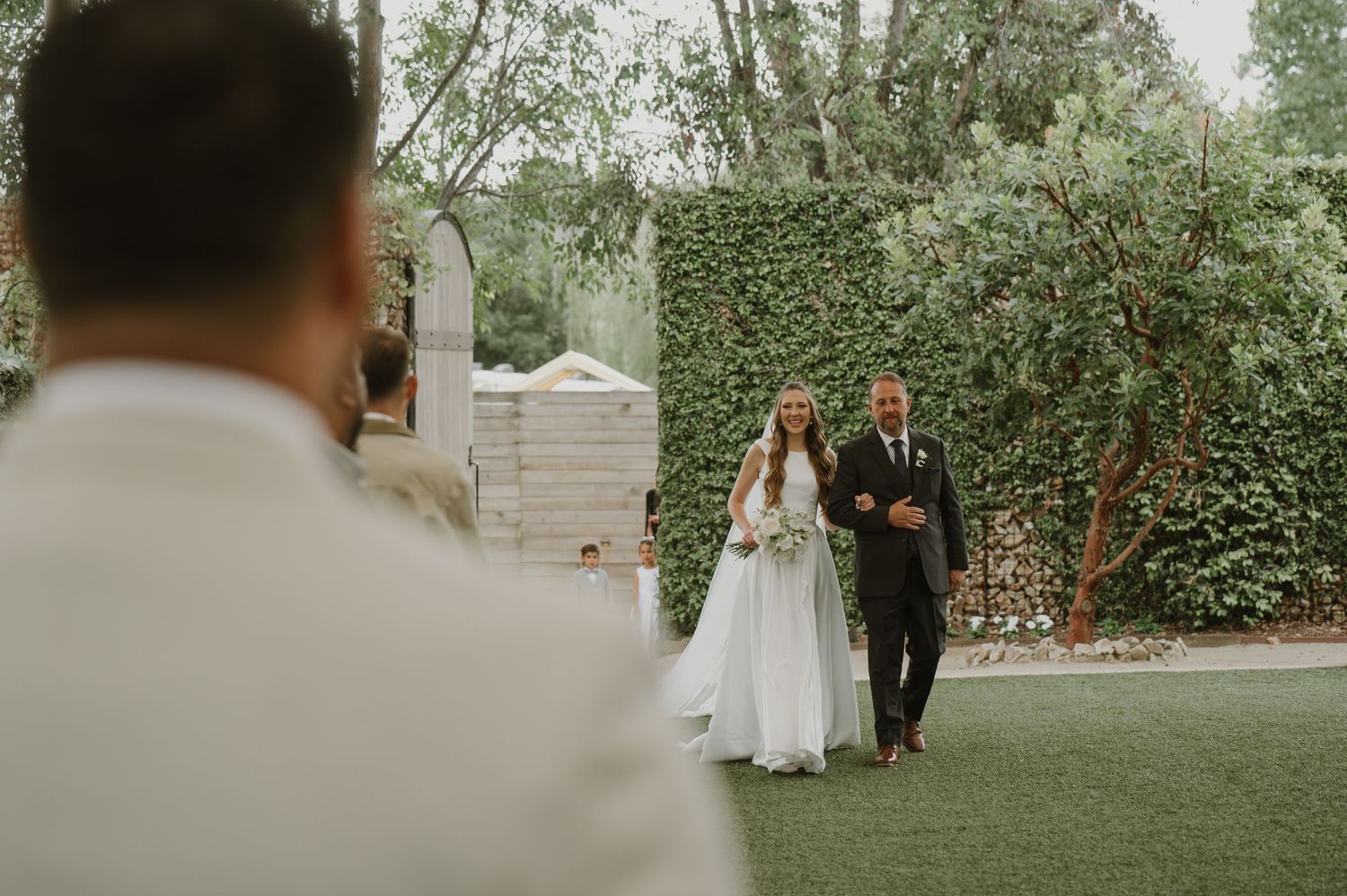 Bride walks down the aisle with her father at an outdoor garden wedding ceremony.