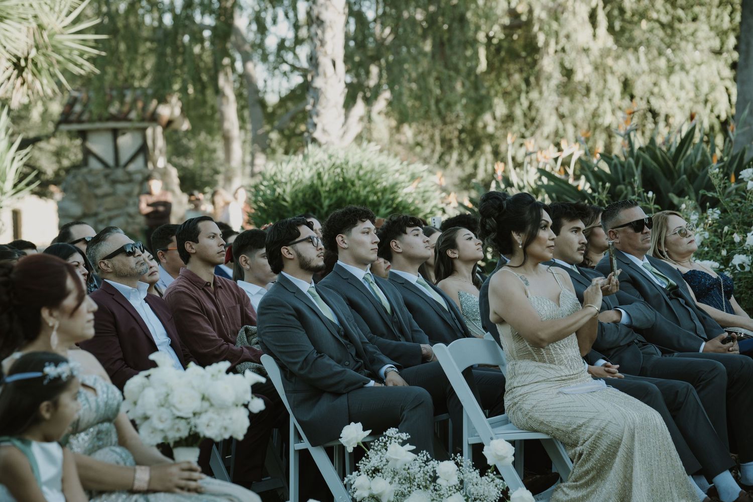 Wedding guests seated in rows during an outdoor ceremony with natural decor.