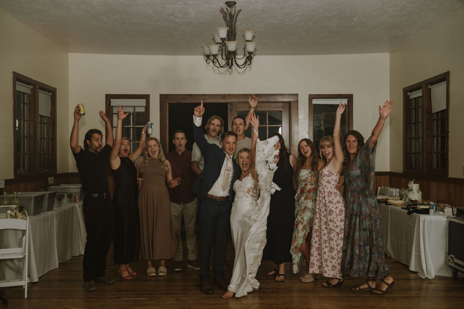 Wedding party and guests dance in line formation at indoor reception venue.