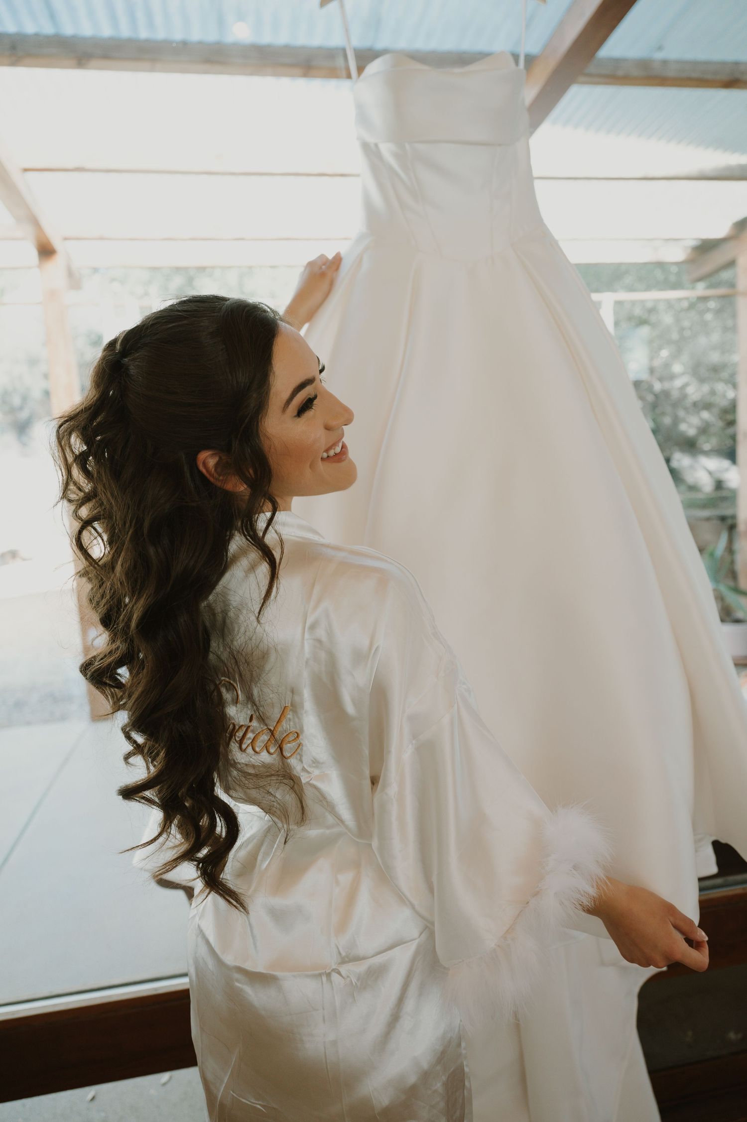 Side view of person in white robe admiring wedding dress on hanger.