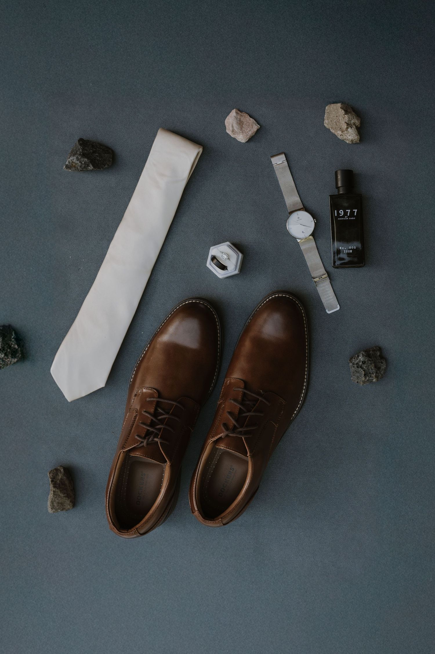 Brown leather dress shoes and accessories arranged on a dark gray background.