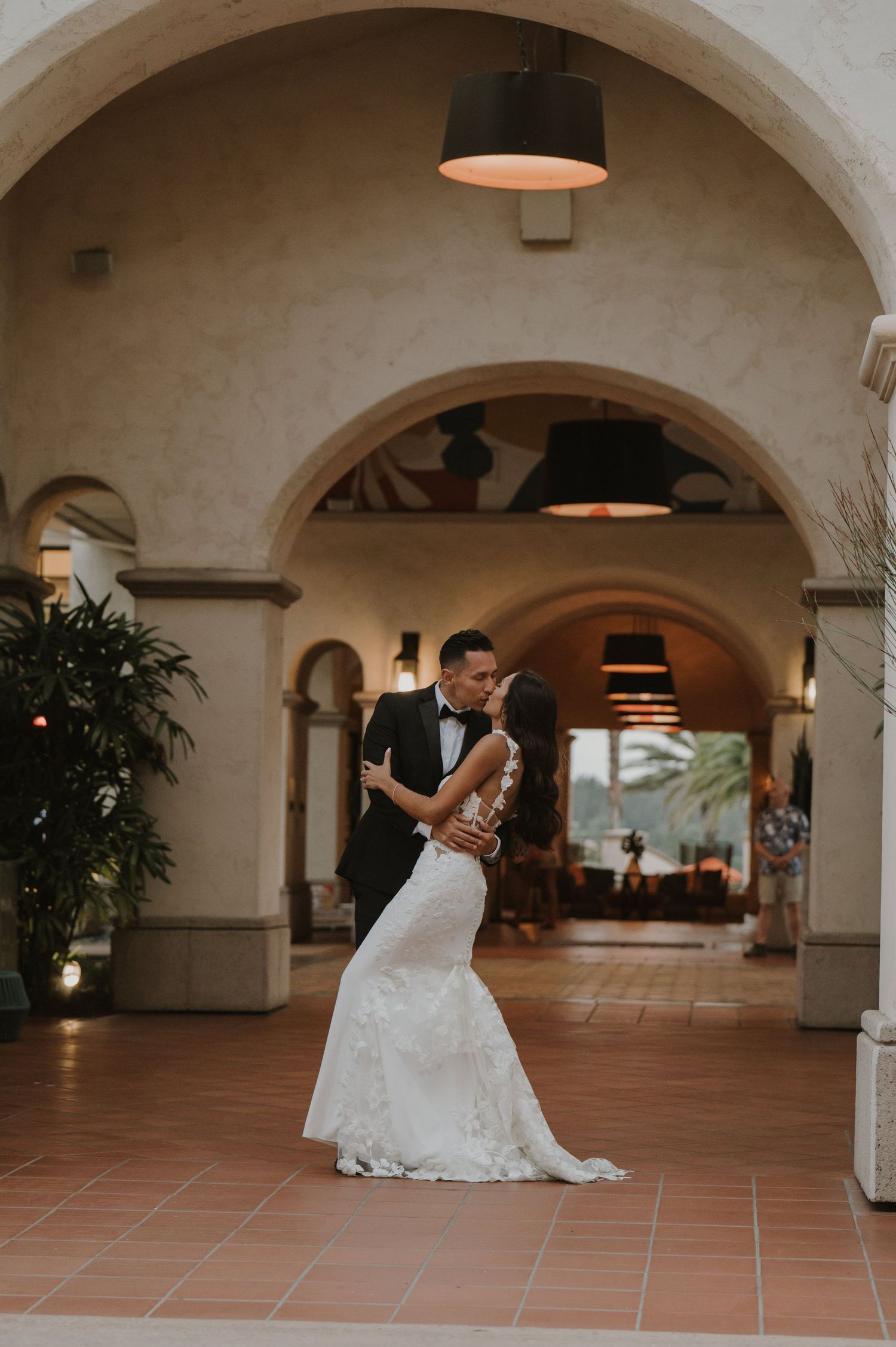 Wedding couple dances beneath arched ceilings in a Mediterranean-style venue with terra cotta floors.