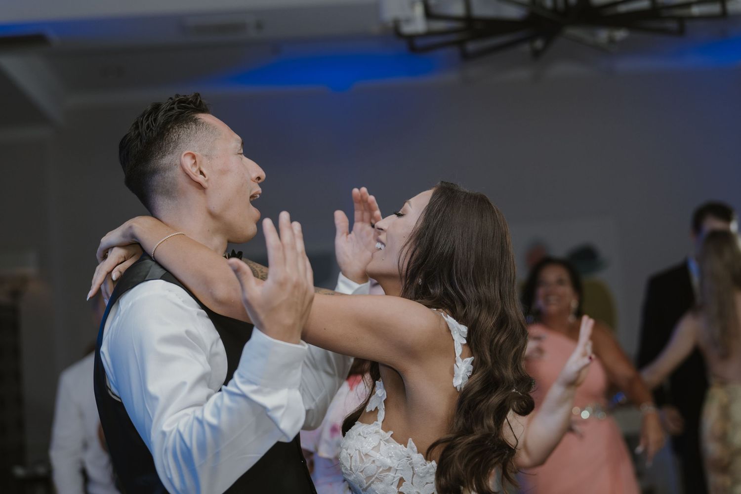 Wedding guests dancing energetically under blue lighting at an indoor reception.