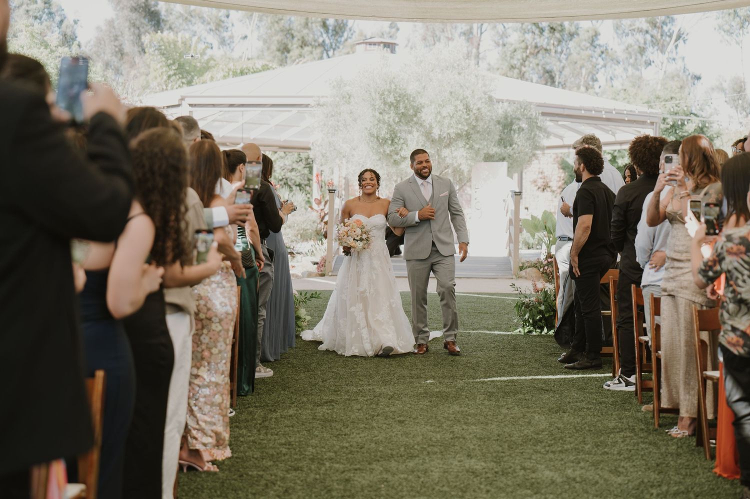 Bride and groom walk back down the aisle after wedding ceremony, guests applauding on both sides.