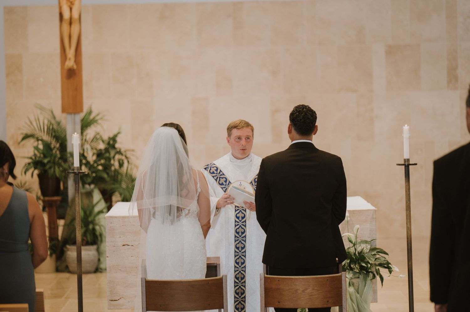 Bride and groom kneel before a priest during a traditional Catholic wedding ceremony at the altar.