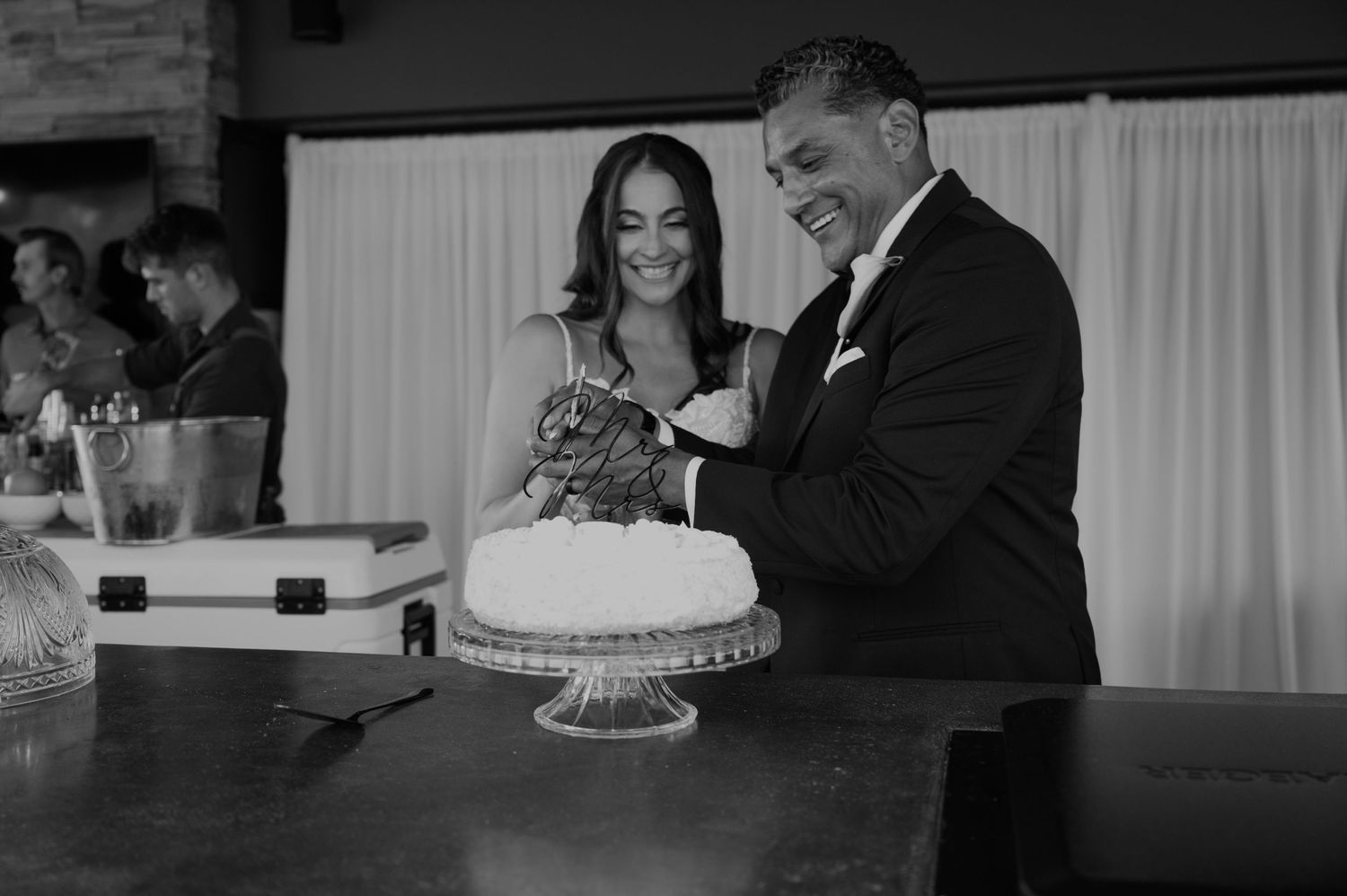 Bride and groom cutting their wedding cake together in black and white photo at elegant indoor reception.