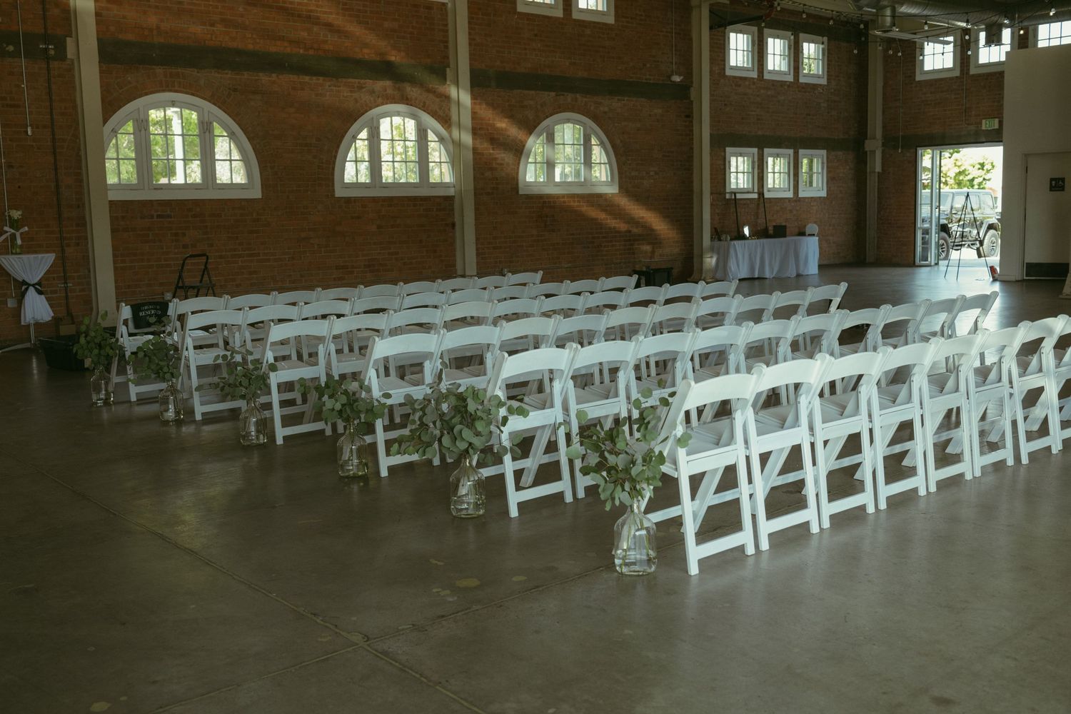 White folding chairs arranged in rows inside a rustic brick wedding venue with arched windows and hardwood floors.