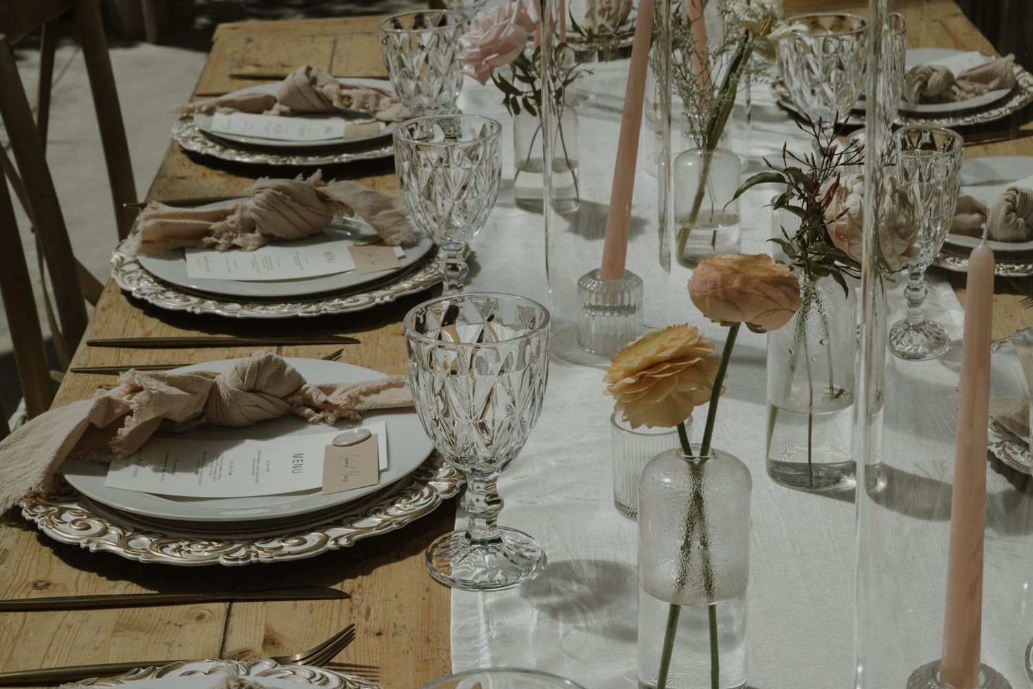 Rustic wedding reception table set with crystal glassware, ornate charger plates, and peach floral arrangements.