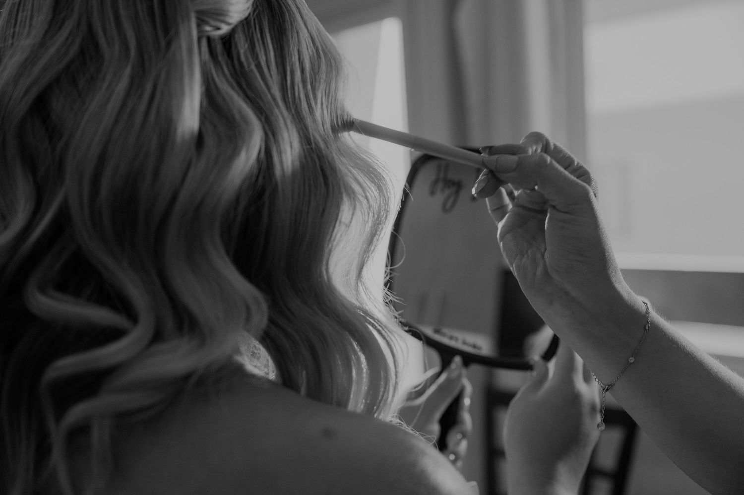 Black and white photo of a woman with curly blonde hair getting makeup applied with a brush.