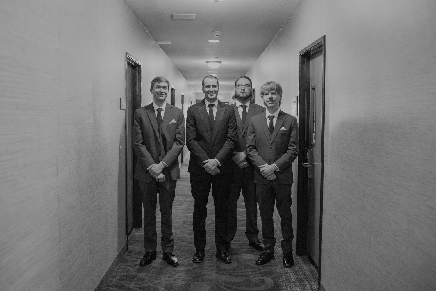 Four men in suits posing together in a hotel hallway, black and white formal group portrait photo.