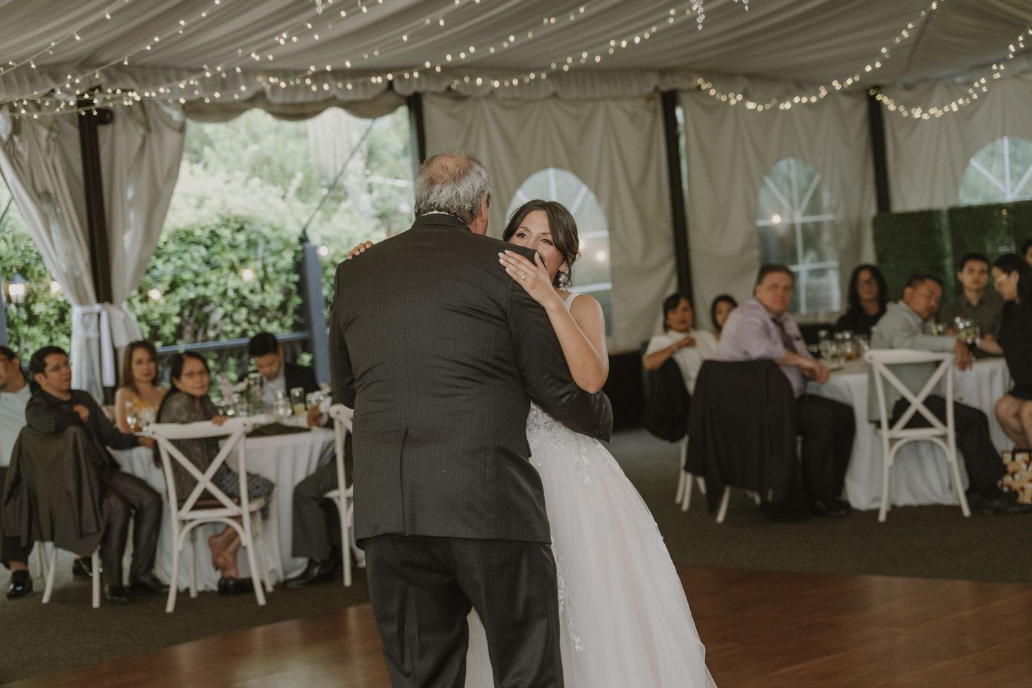 Bride and father share emotional first dance under fairy lights at wedding reception.
