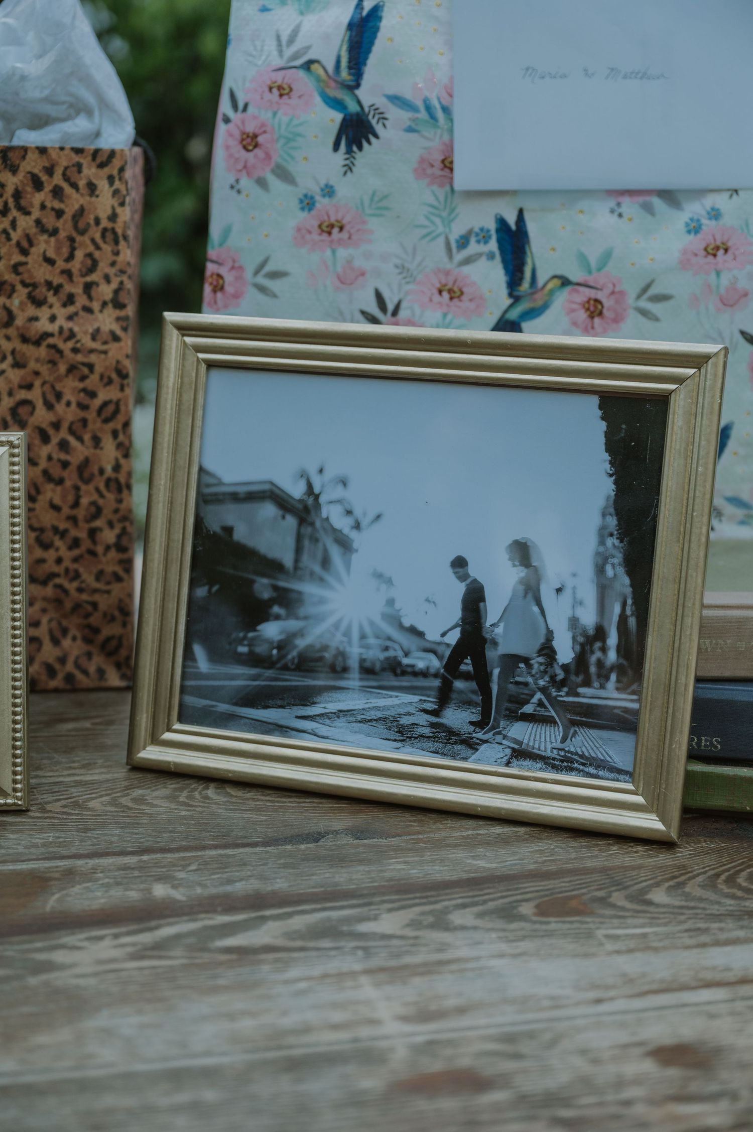 Framed black and white engagement photo displayed on a wooden table with floral gift bags at a wedding.