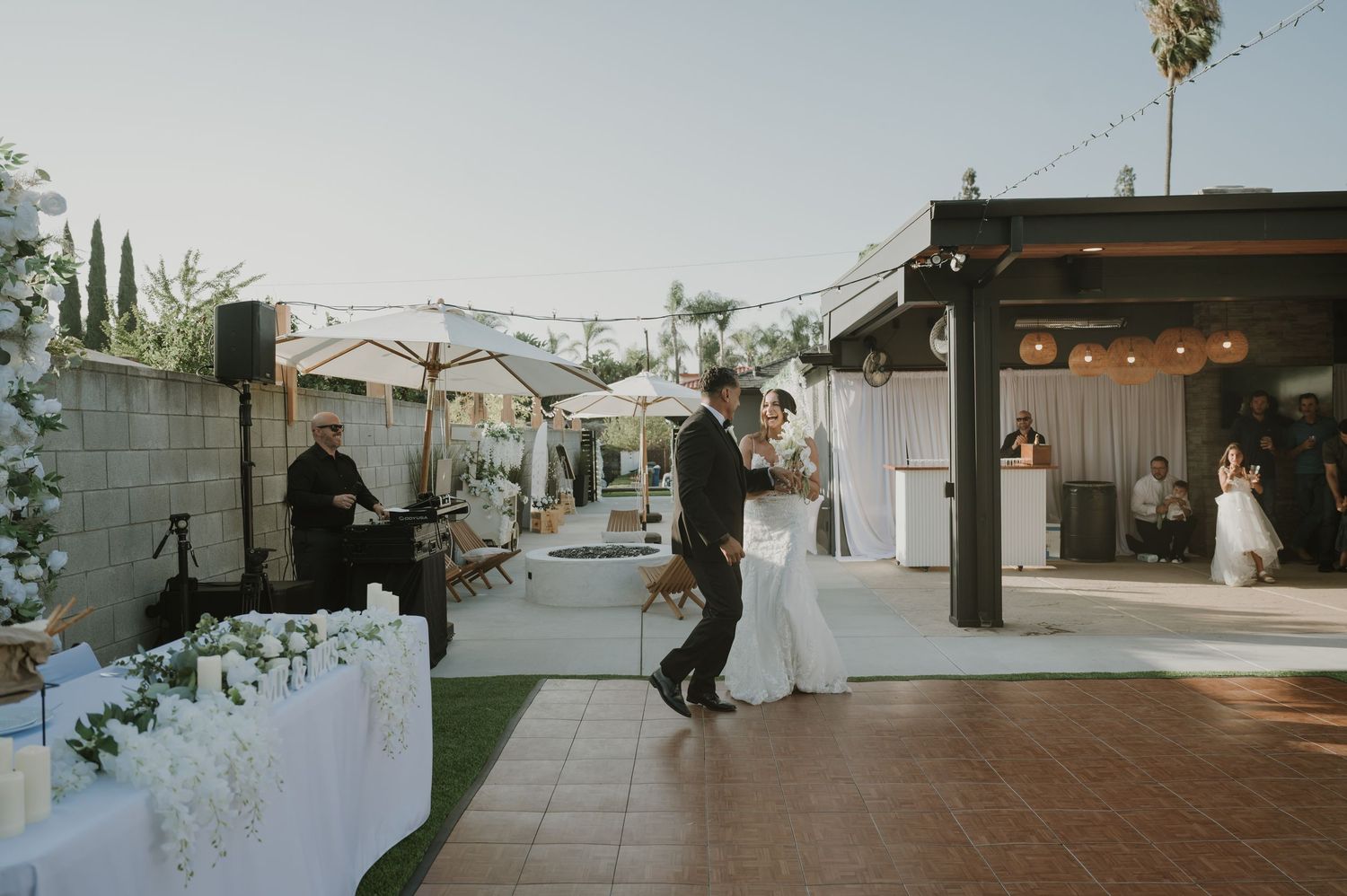 Couple shares first dance at elegant outdoor wedding reception with string lights and white floral decorations.