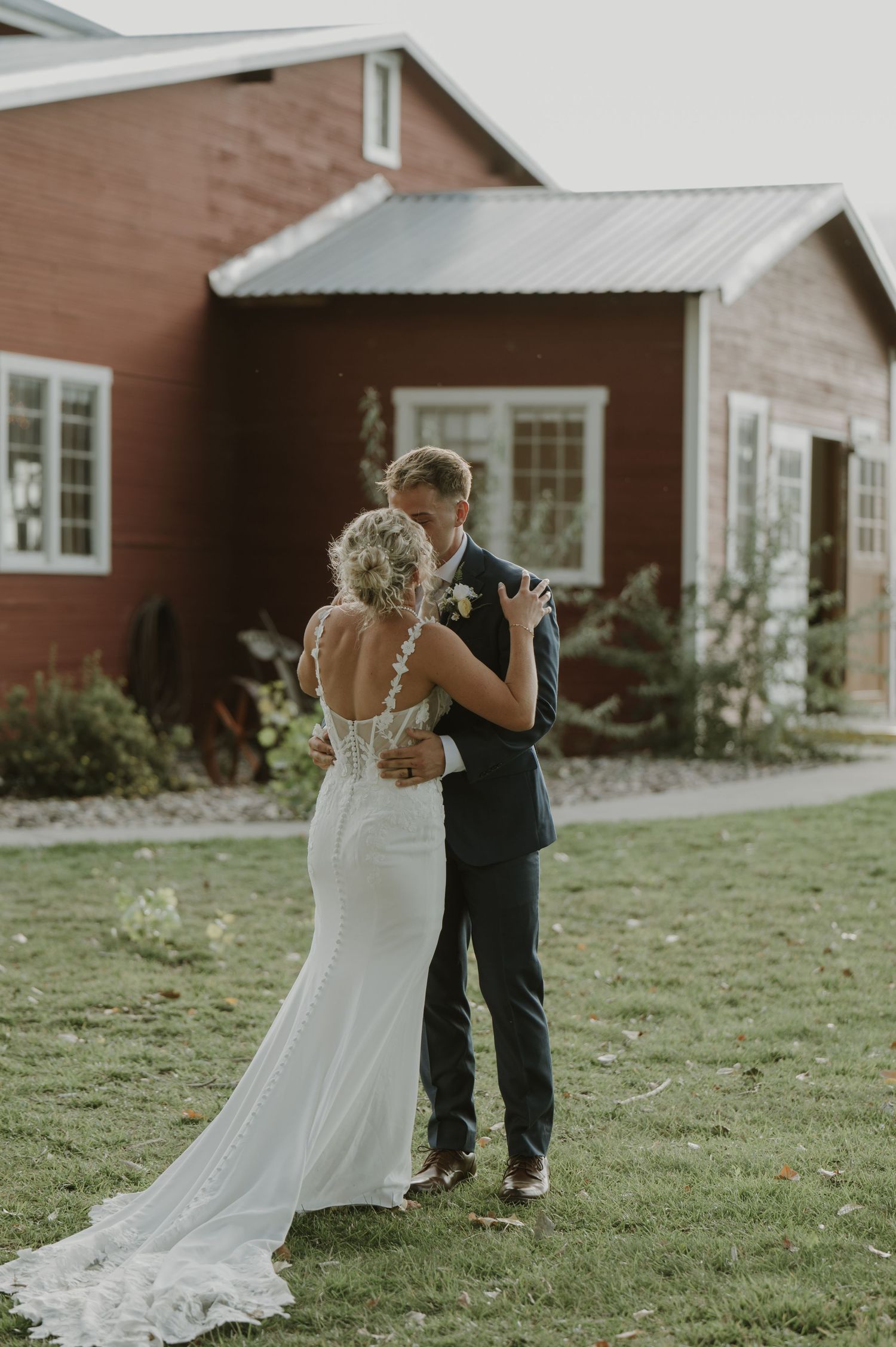 A couple shares a tender first look moment in front of a rustic red barn on their wedding day.