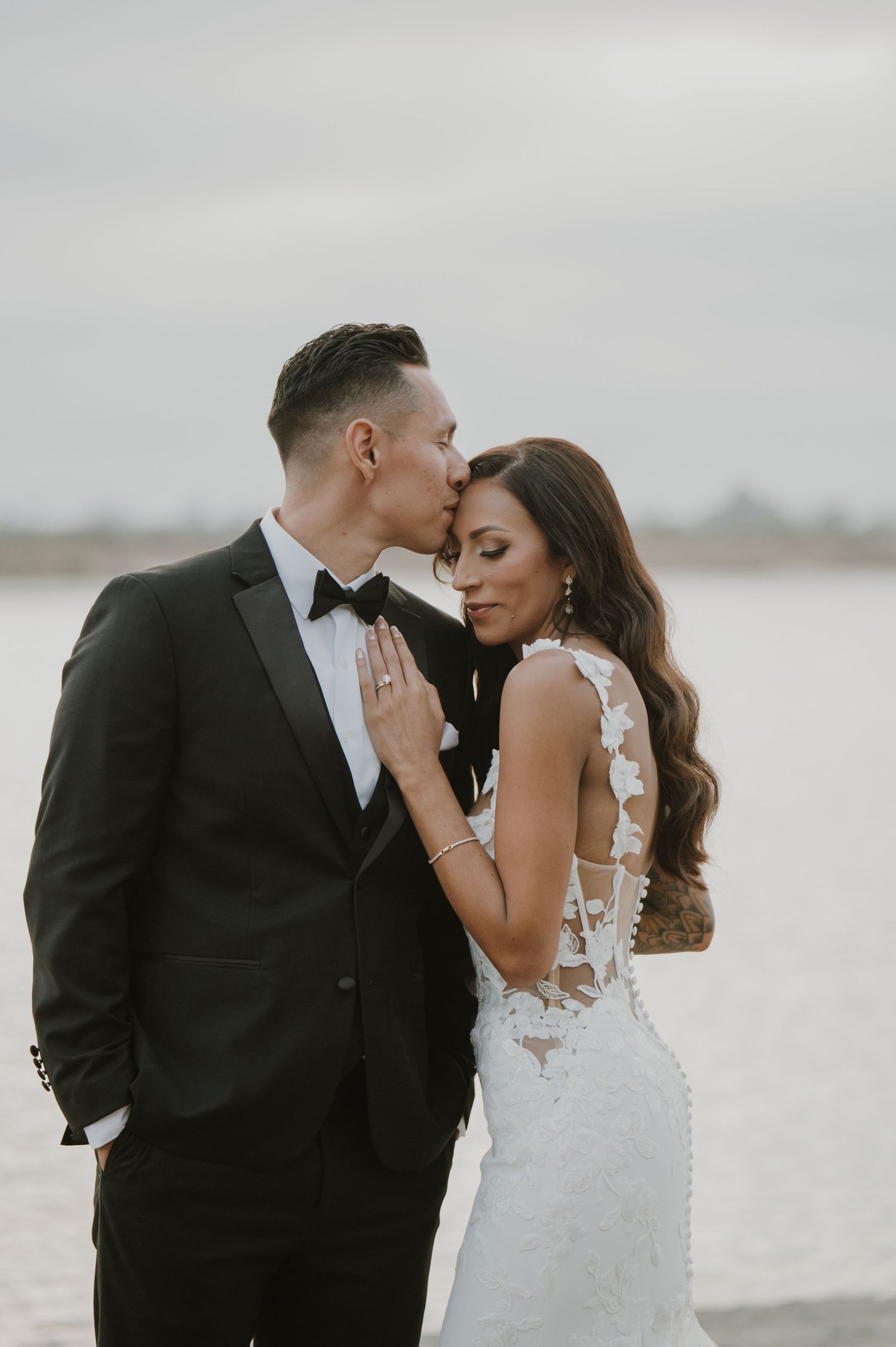 An intimate moment between newlyweds on a beach with moody gray skies in the background.