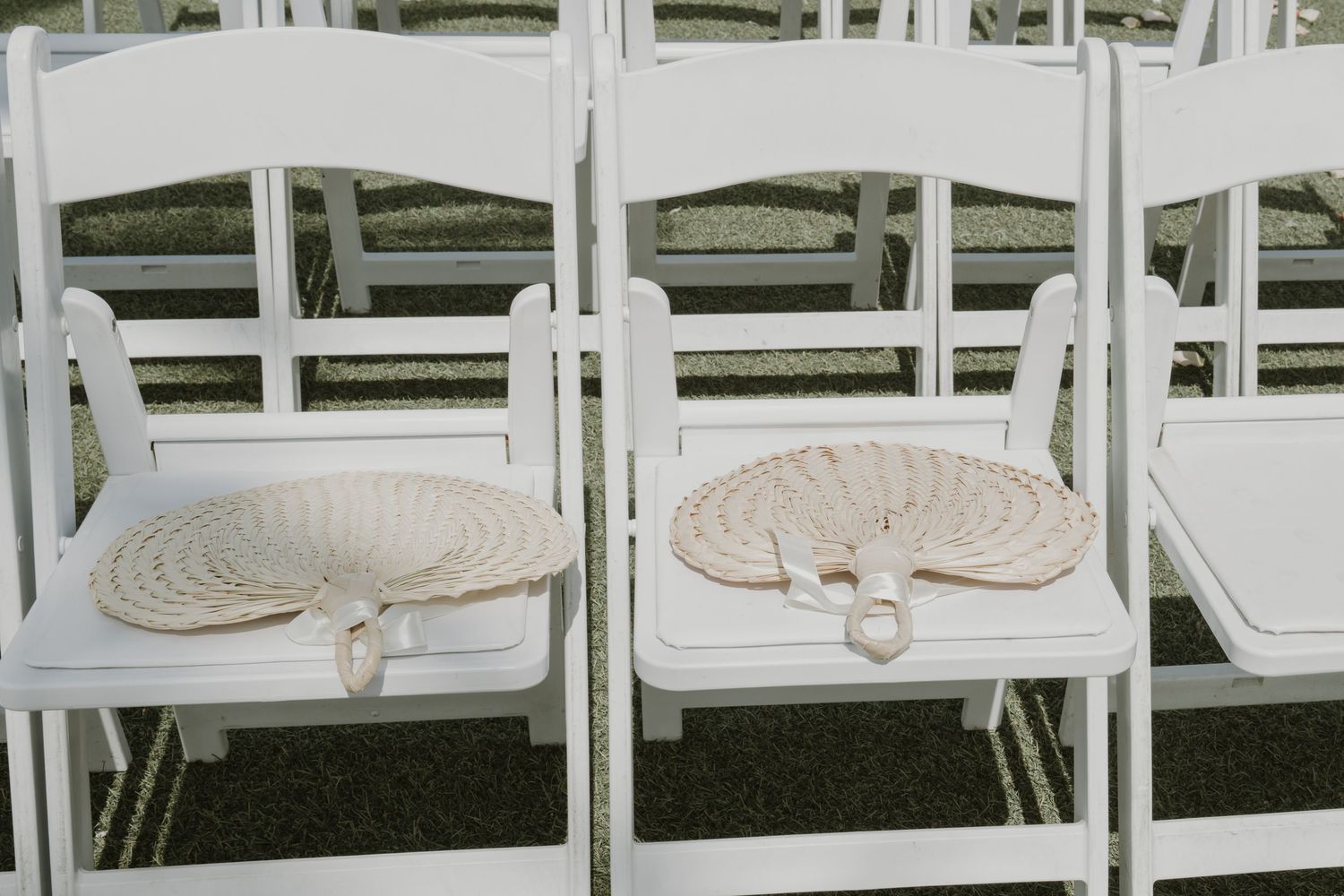 Row of white folding chairs set up for an outdoor ceremony.