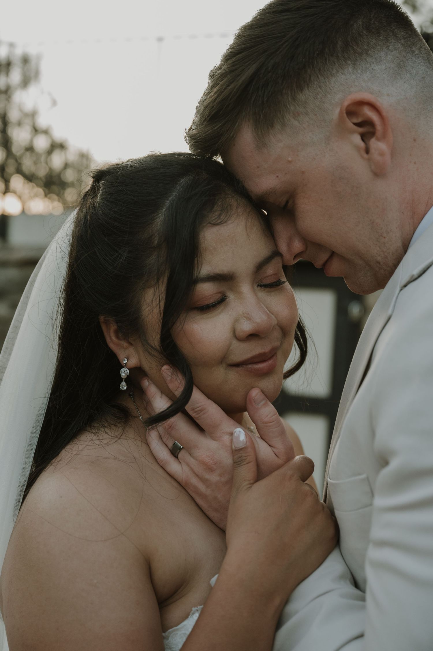 Groom tenderly holds brides face as they share an intimate forehead-to-forehead moment.