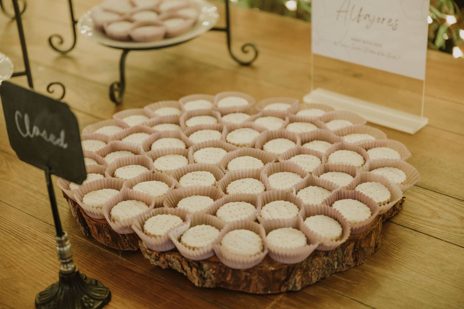 Rows of pink macarons in white cupcake liners displayed on a rustic wood slice at a wedding dessert table.