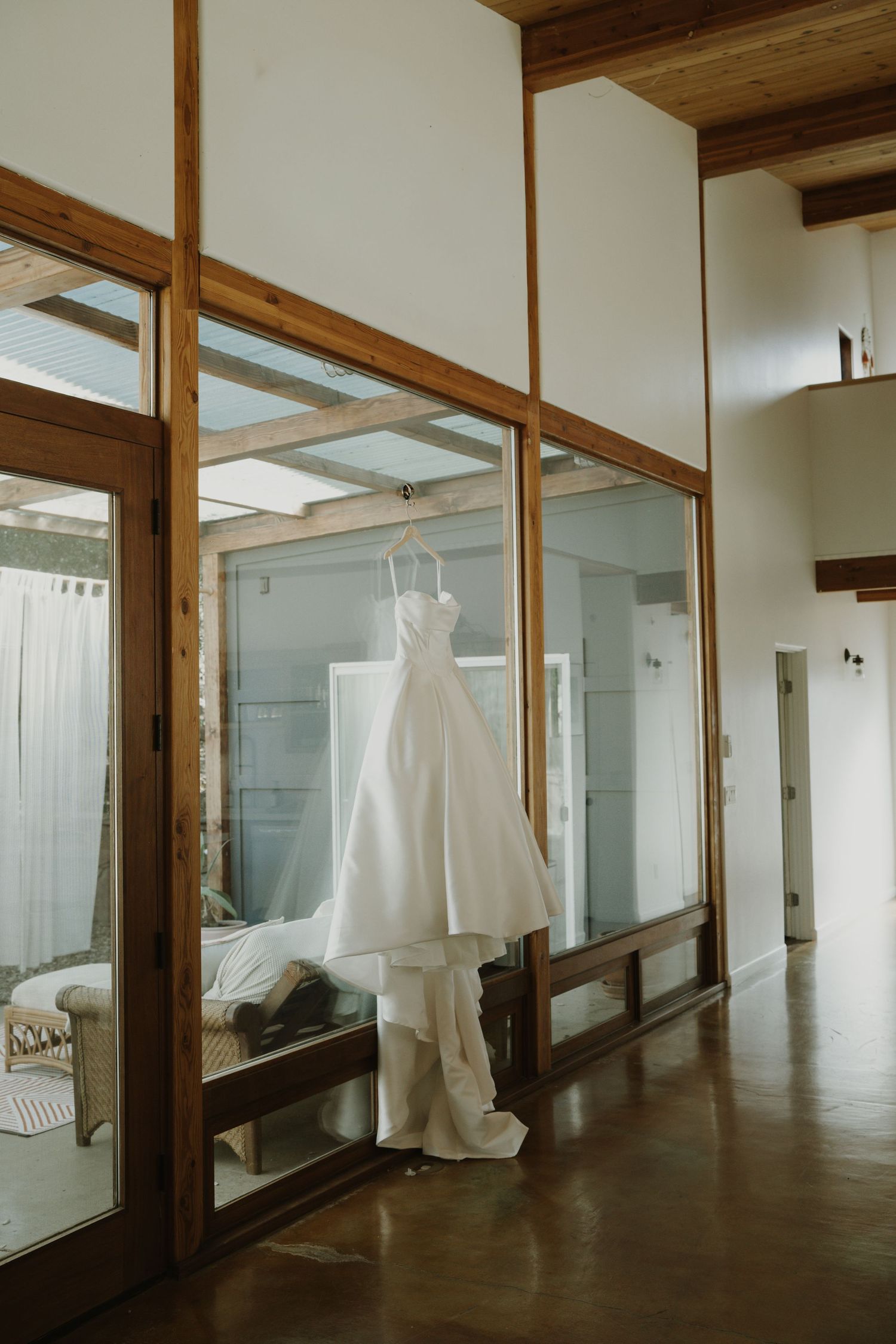 Wedding dress displayed in a modern room with wooden beams and mirrored walls.