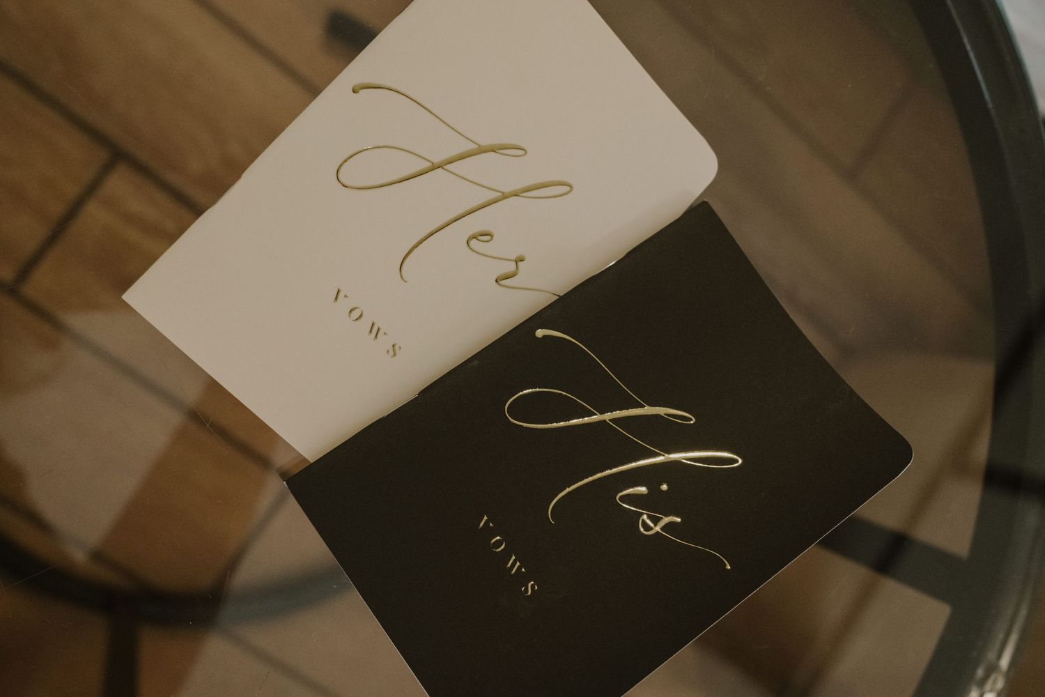 His and hers wedding vow books in black and white on wooden surface.