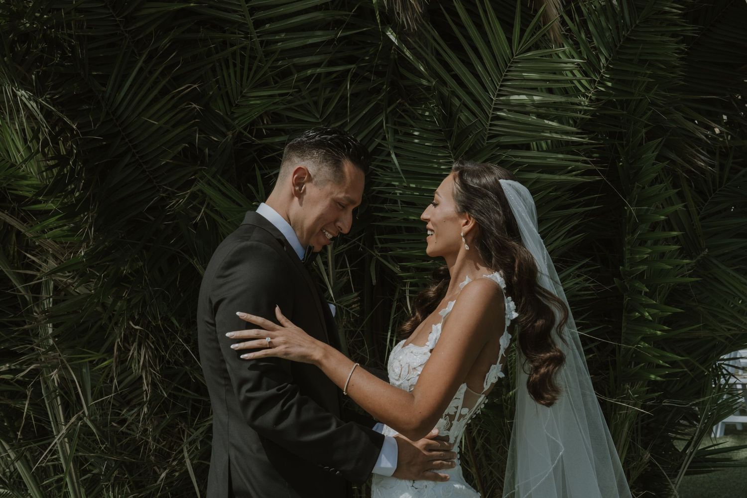 A romantic wedding portrait showing a couple embracing under palm trees in an intimate moment.