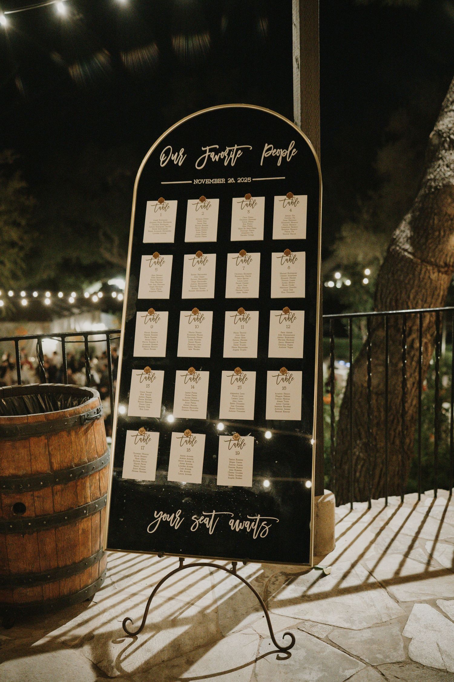 Wedding seating chart displayed on black boards with string lights and wine barrel decor.