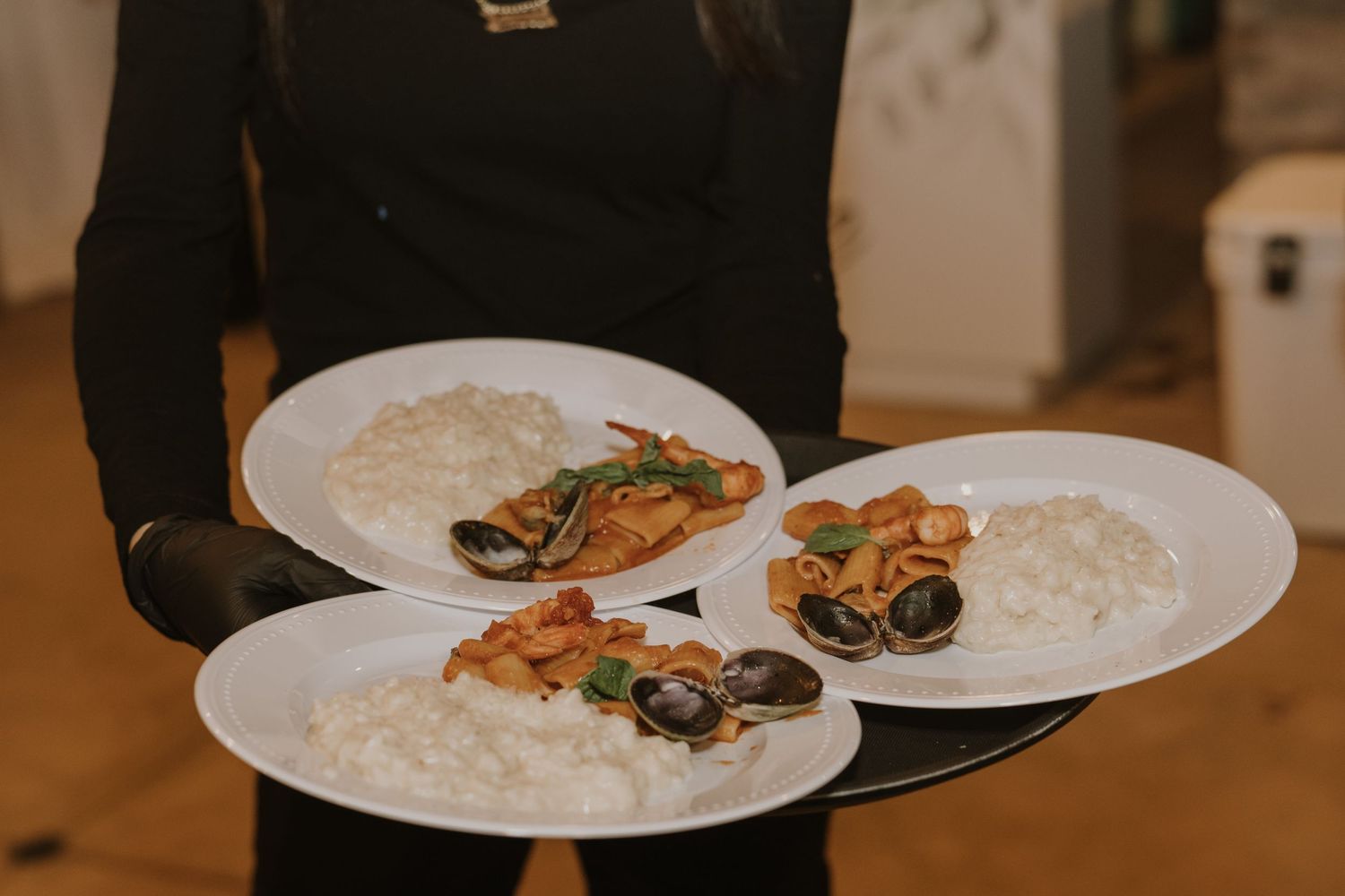 Waiter in black gloves serving three white plates of seafood with rice at a catered event.