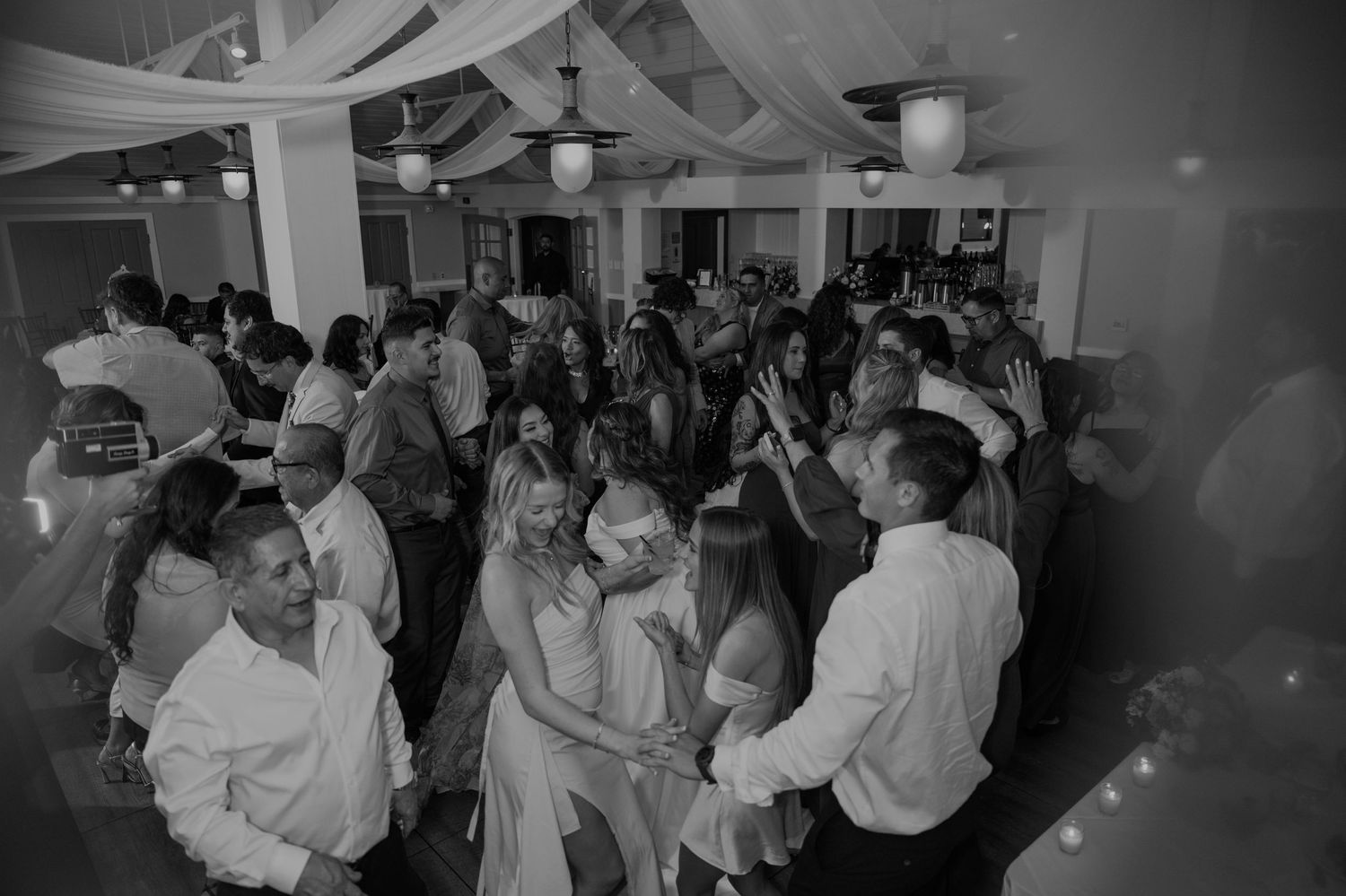 Black and white photo of a crowded wedding reception dance floor with bride and guests dancing.