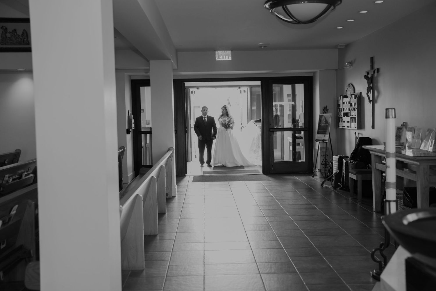 Bride and groom walking down church hallway in black and white wedding photo.