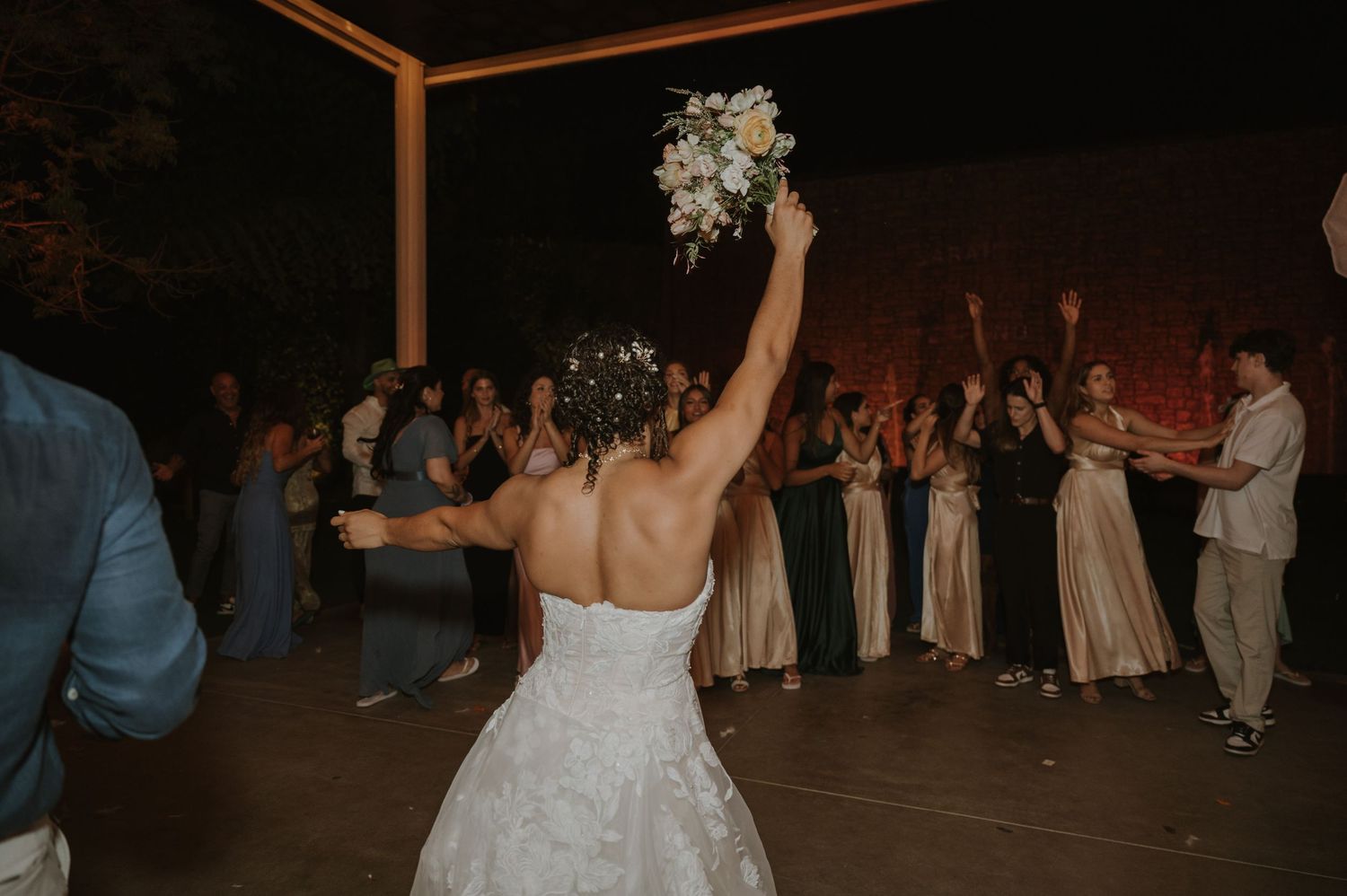 A bride raises her bouquet before the bouquet toss at her outdoor evening wedding reception.