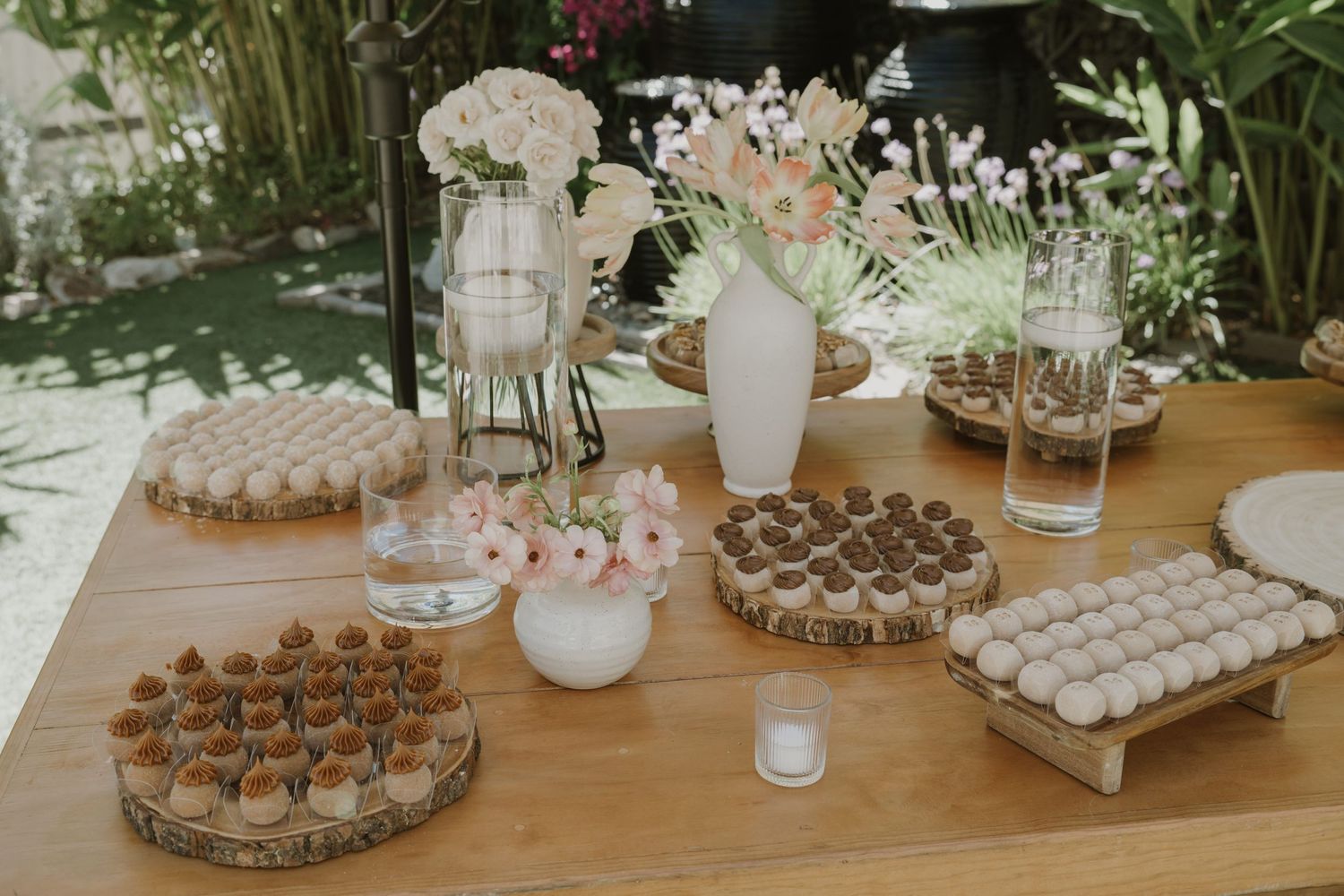 Rustic wooden dessert table displaying assorted macarons and treats on tree slice platters with floral arrangements.