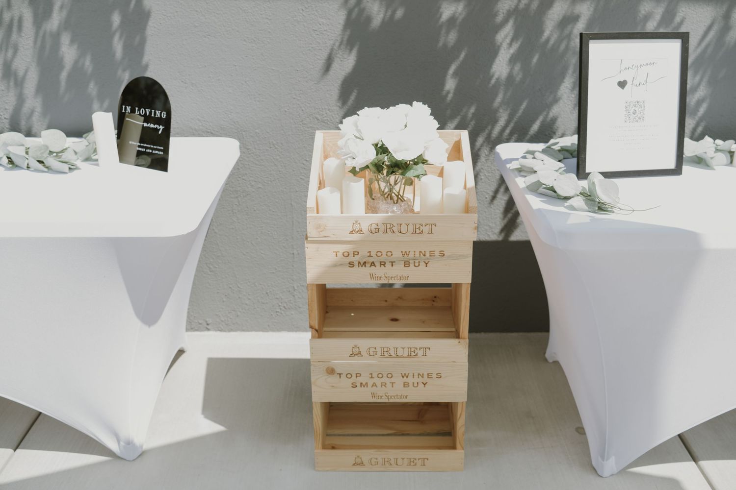 Rustic wooden wine crates stacked as a display stand with white floral arrangement at an elegant outdoor wedding reception.