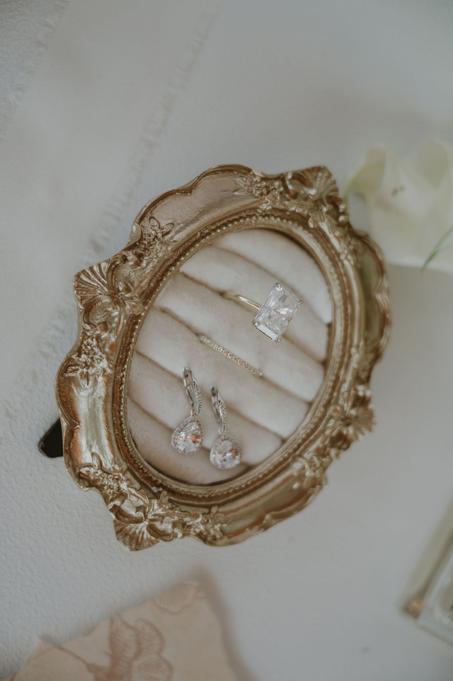Elegant gold ornate oval frame jewelry dish displaying crystal drop earrings and diamond rings on cream velvet.