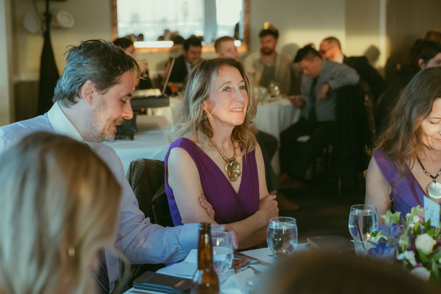 Guests smiling and chatting at a wedding reception dinner table in a warmly lit venue.