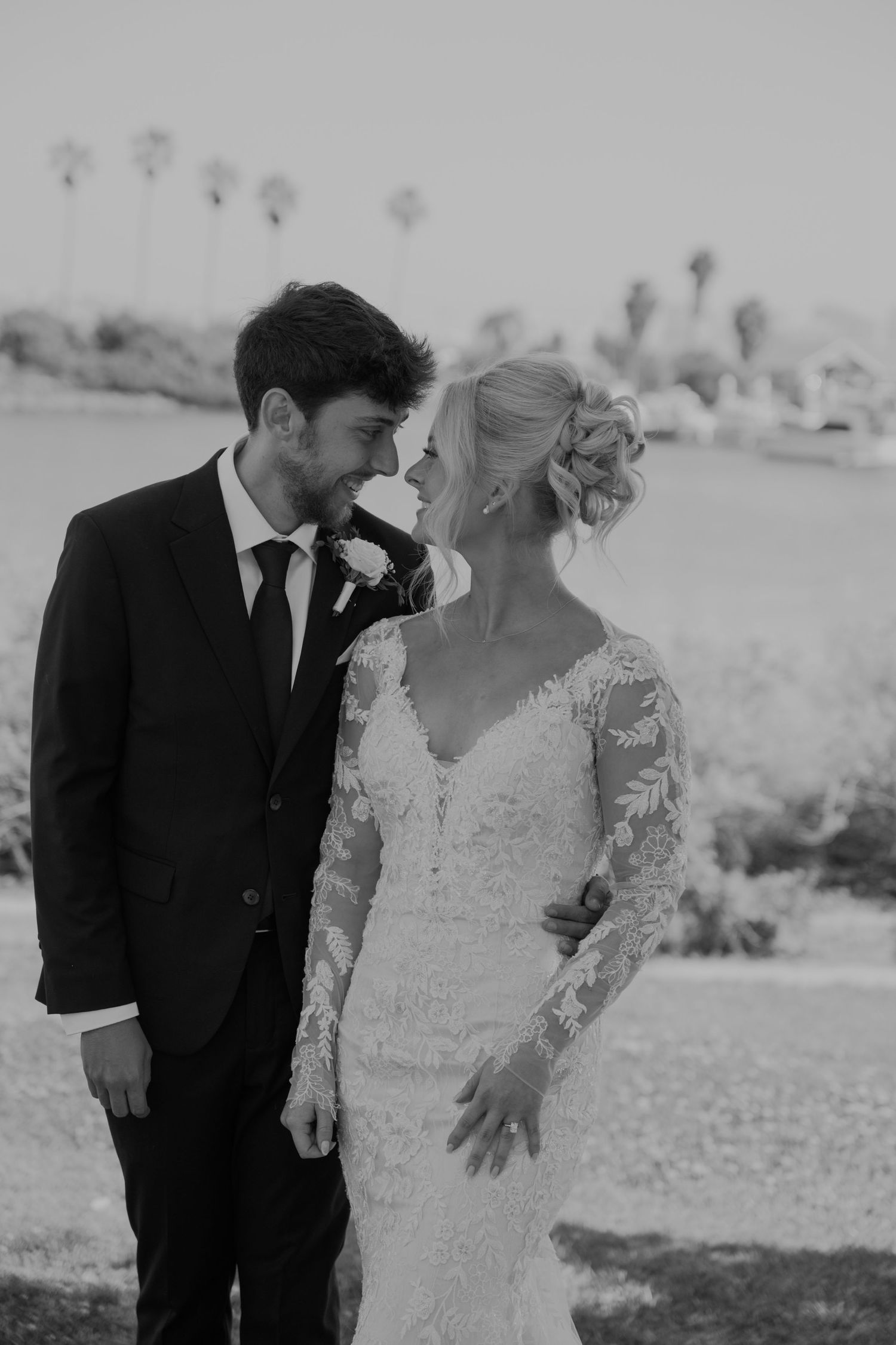 Black and white photo of bride and groom sharing an intimate moment, bride in lace gown with palm trees background.