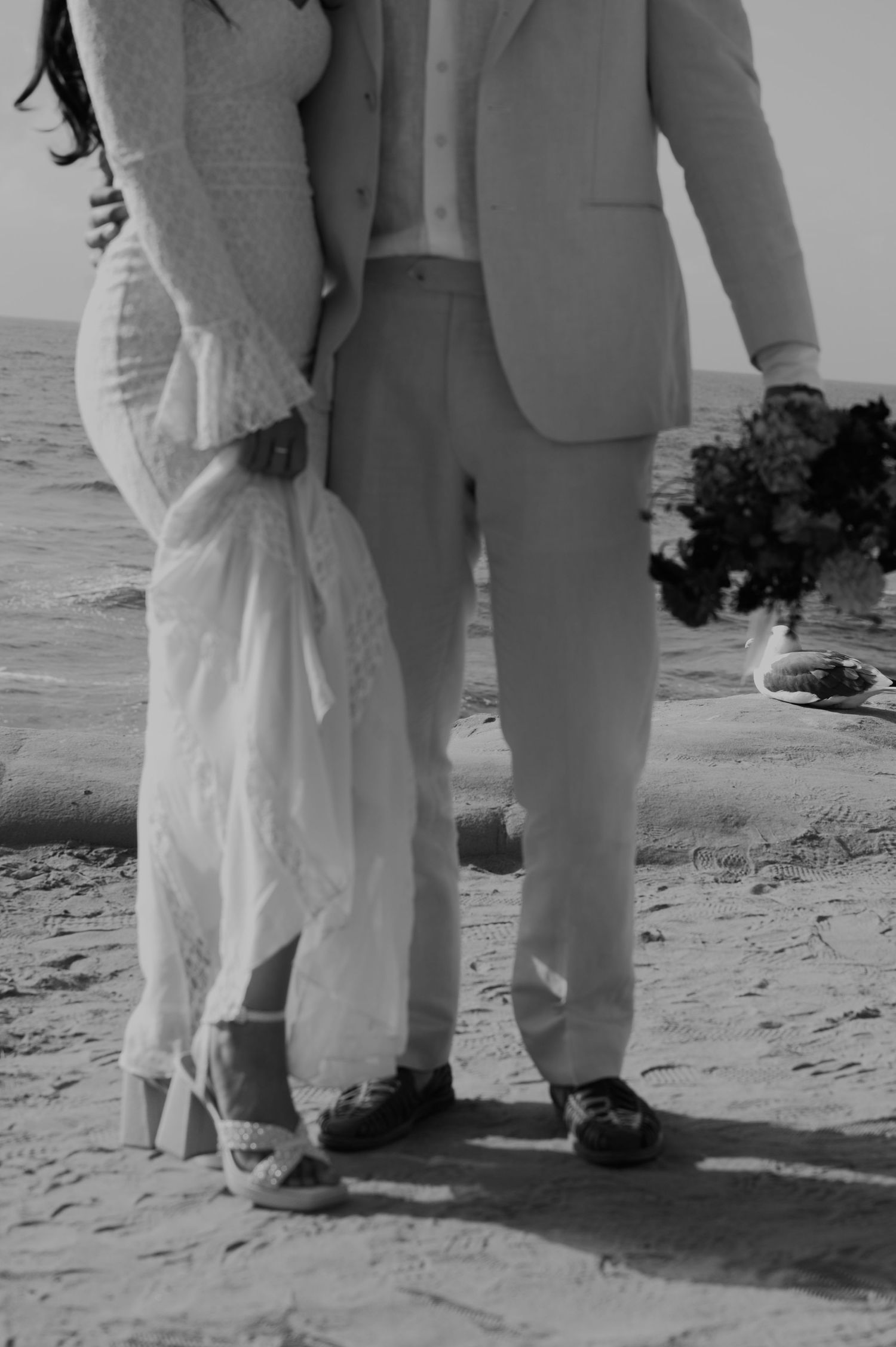 A black and white photo showing the feet of people standing on a beach.
