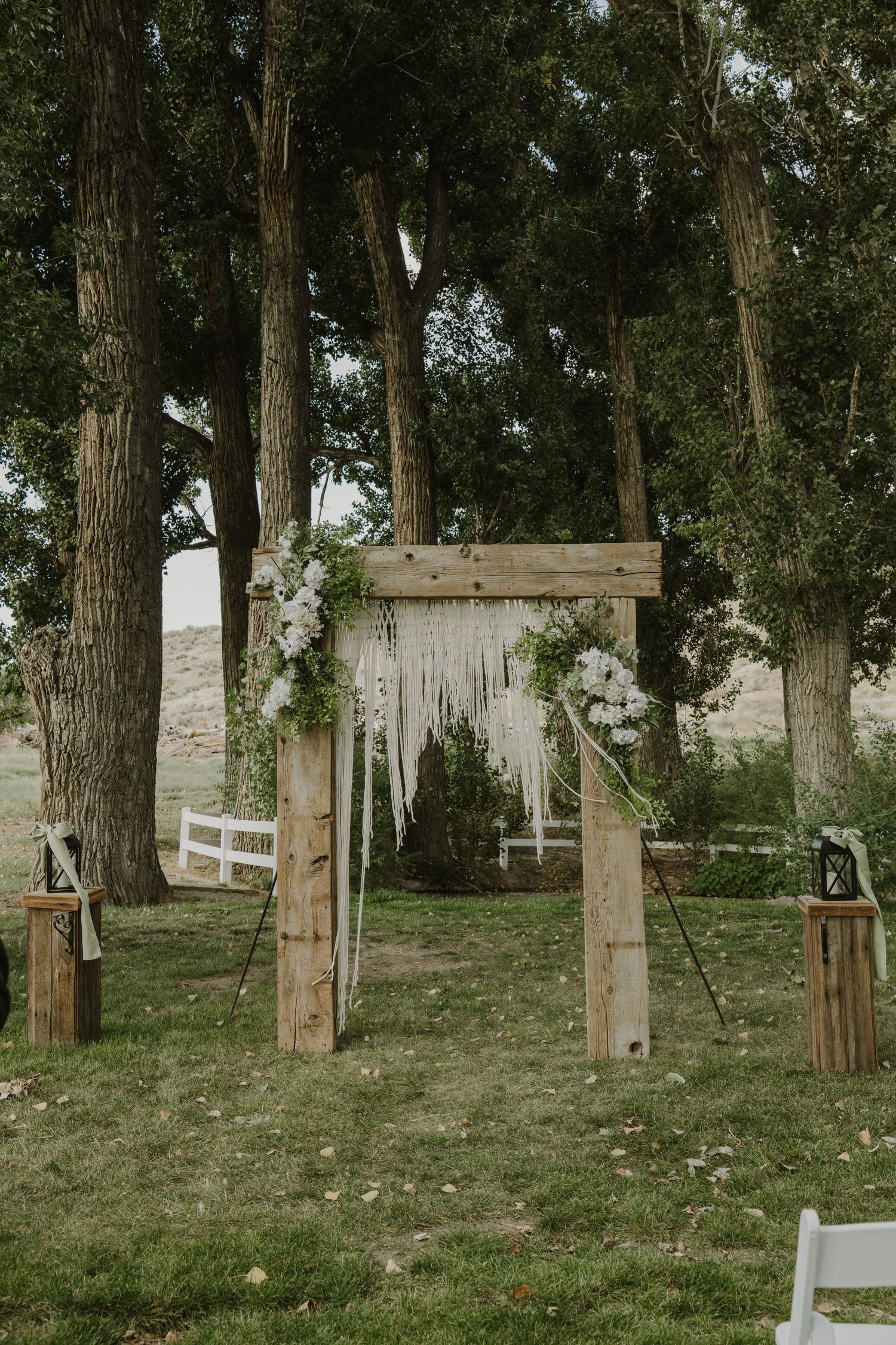 Rustic outdoor wedding ceremony setup with wooden posts and white fabric decorations among tall trees.