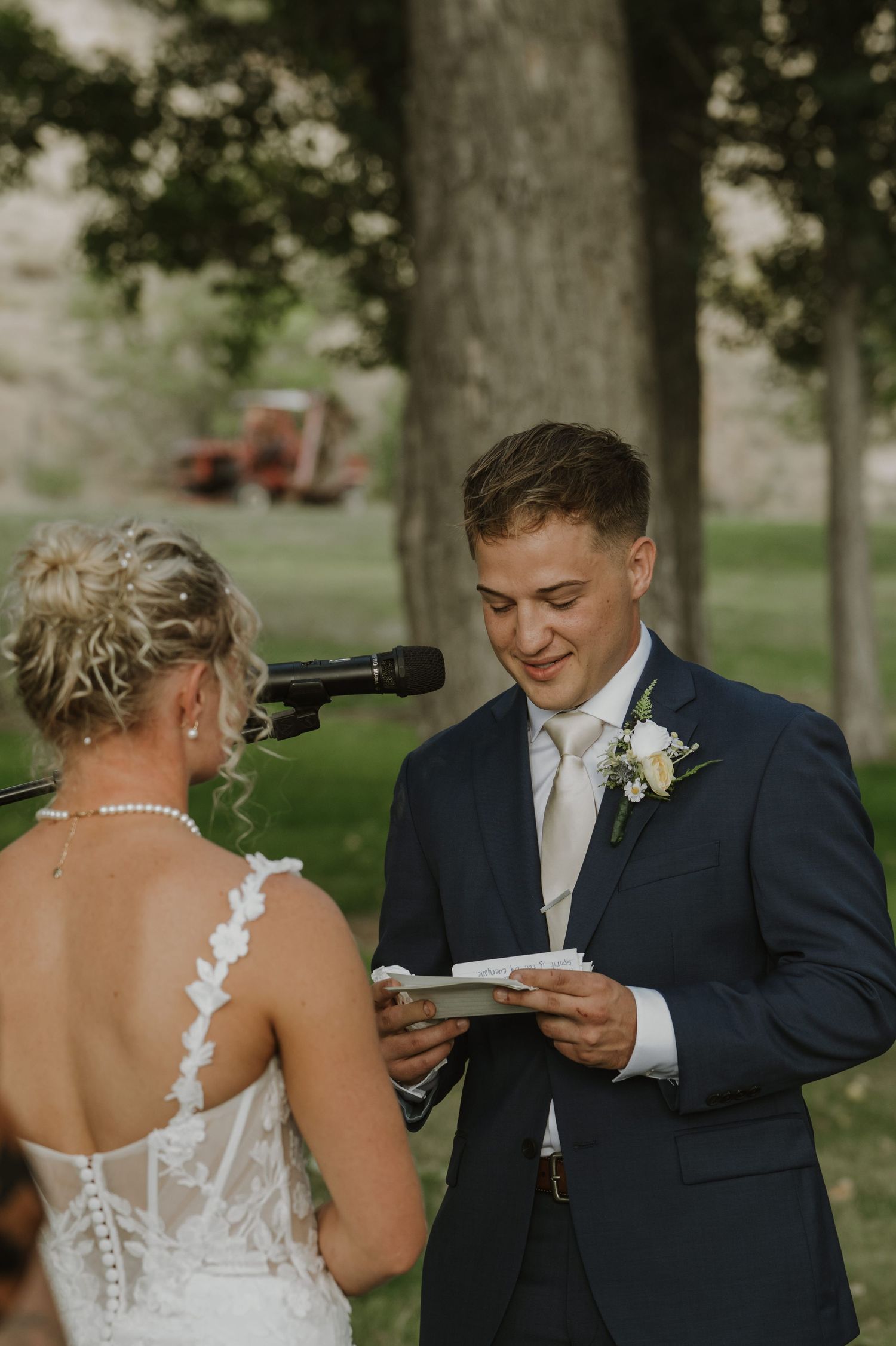 Wedding couple exchanging vows during intimate outdoor ceremony under tall trees.